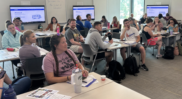 Large group of Drake University students sitting at tables in a classroom listening to a lecture.