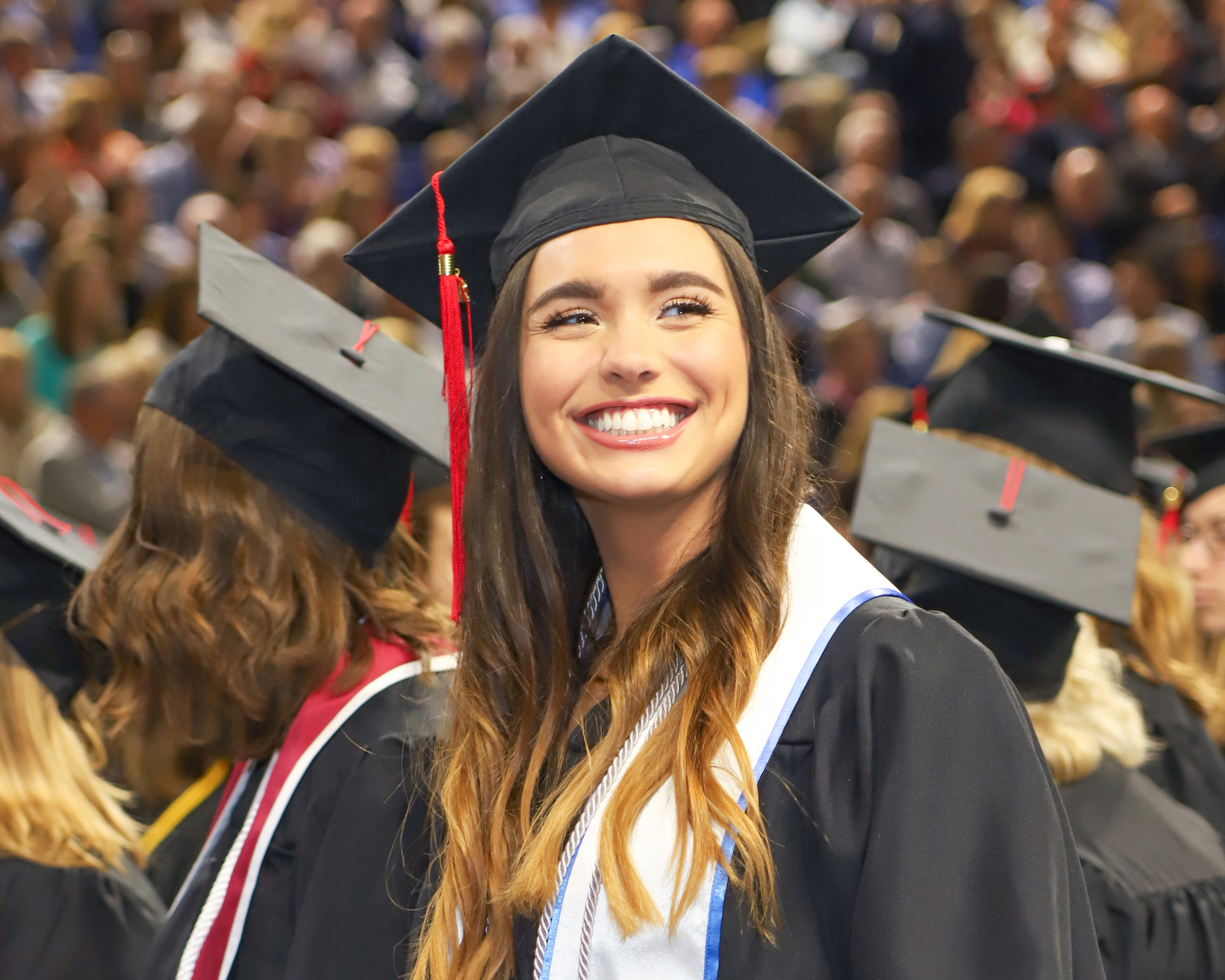 A Drake student in a cap, gown, and honors sash looks back at the crowd during commencement