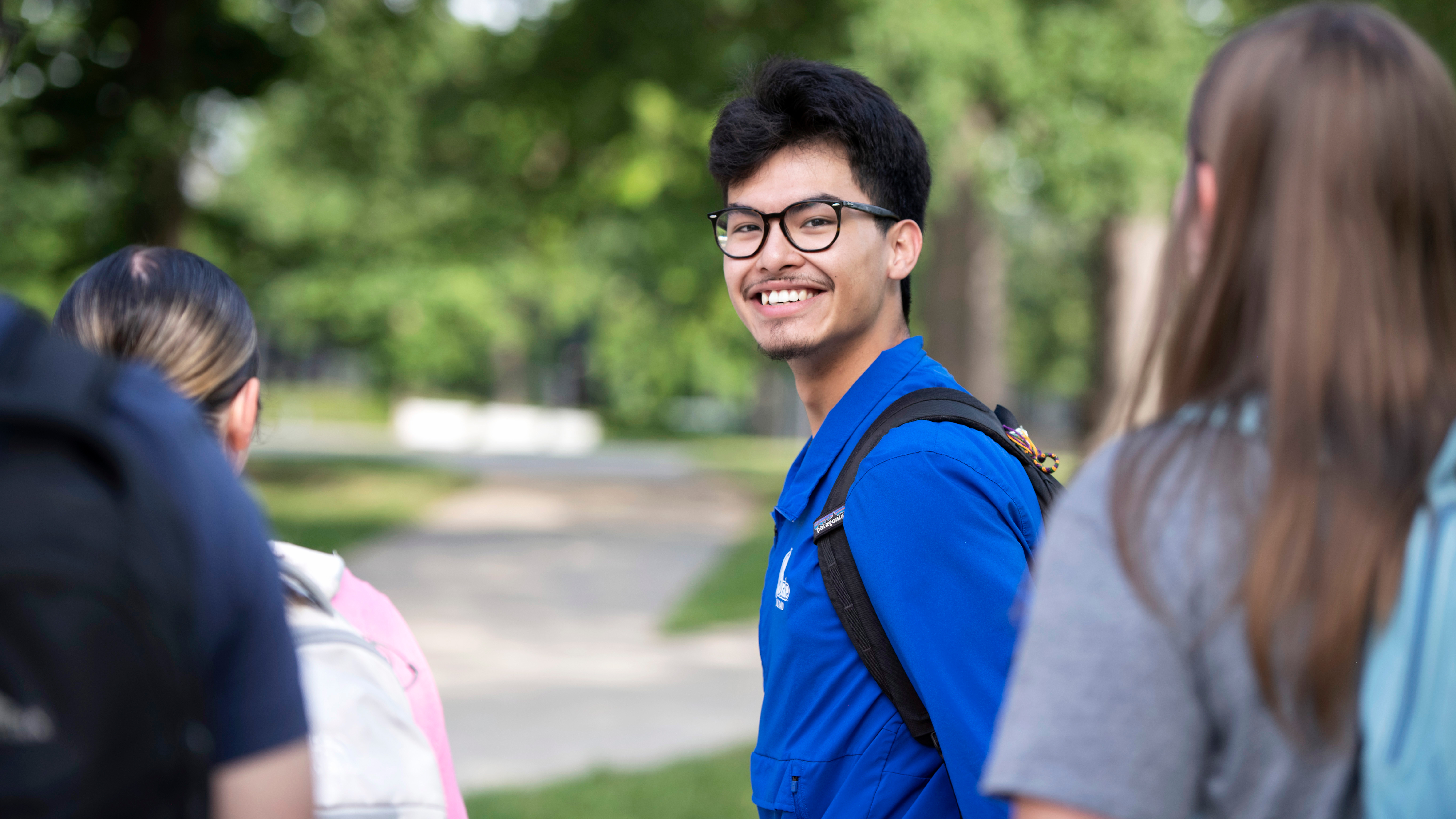 A Drake student with a backpack smiles while looking back at their tour group