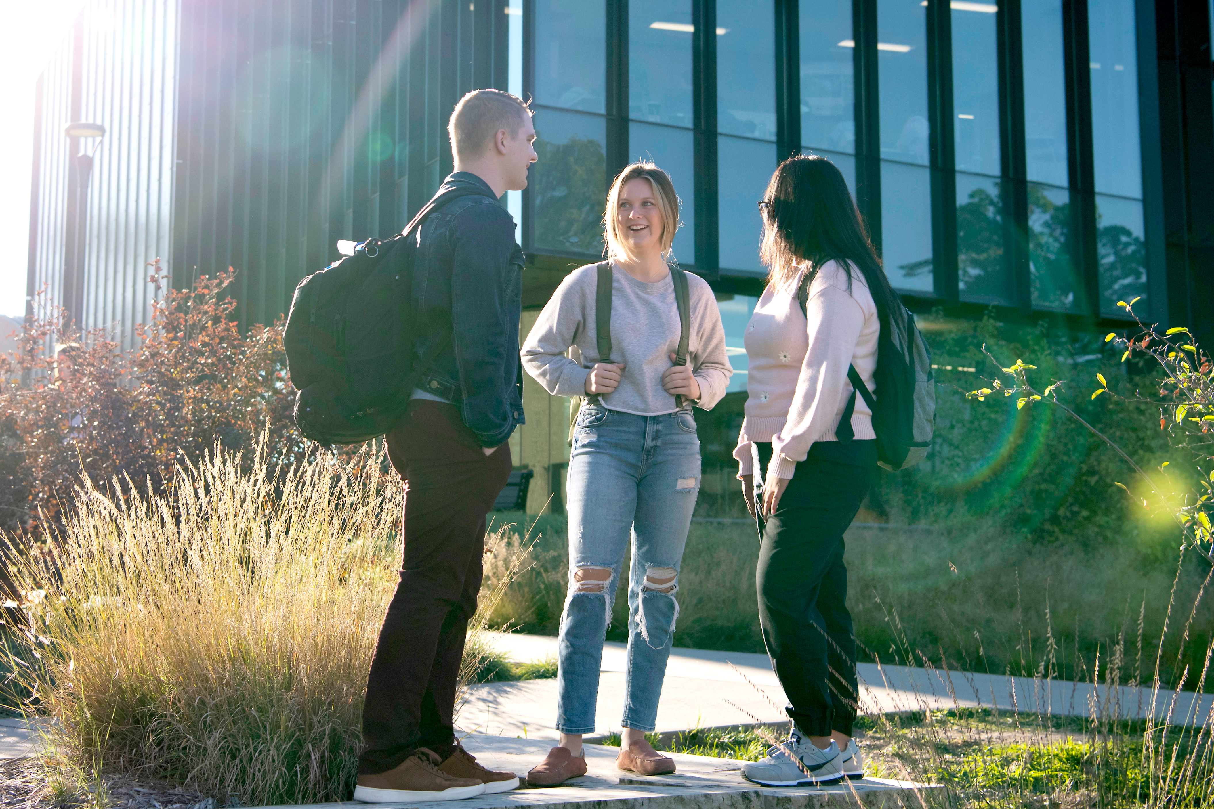 A group of Drake students converse outside a classroom building with large windows