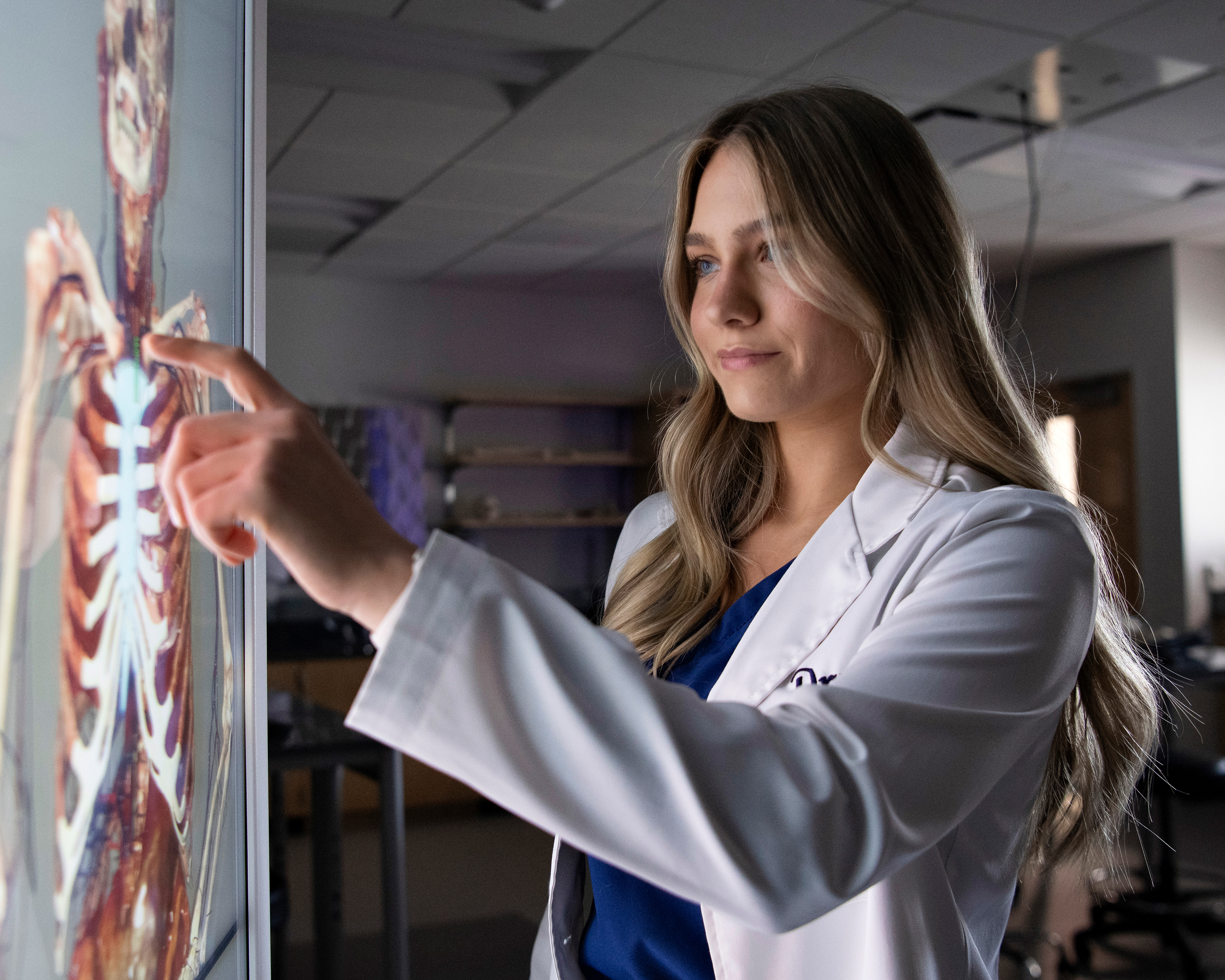 In a dark campus lab, a Drake students adjusts an anatomage table with their finger to learn more about the human body