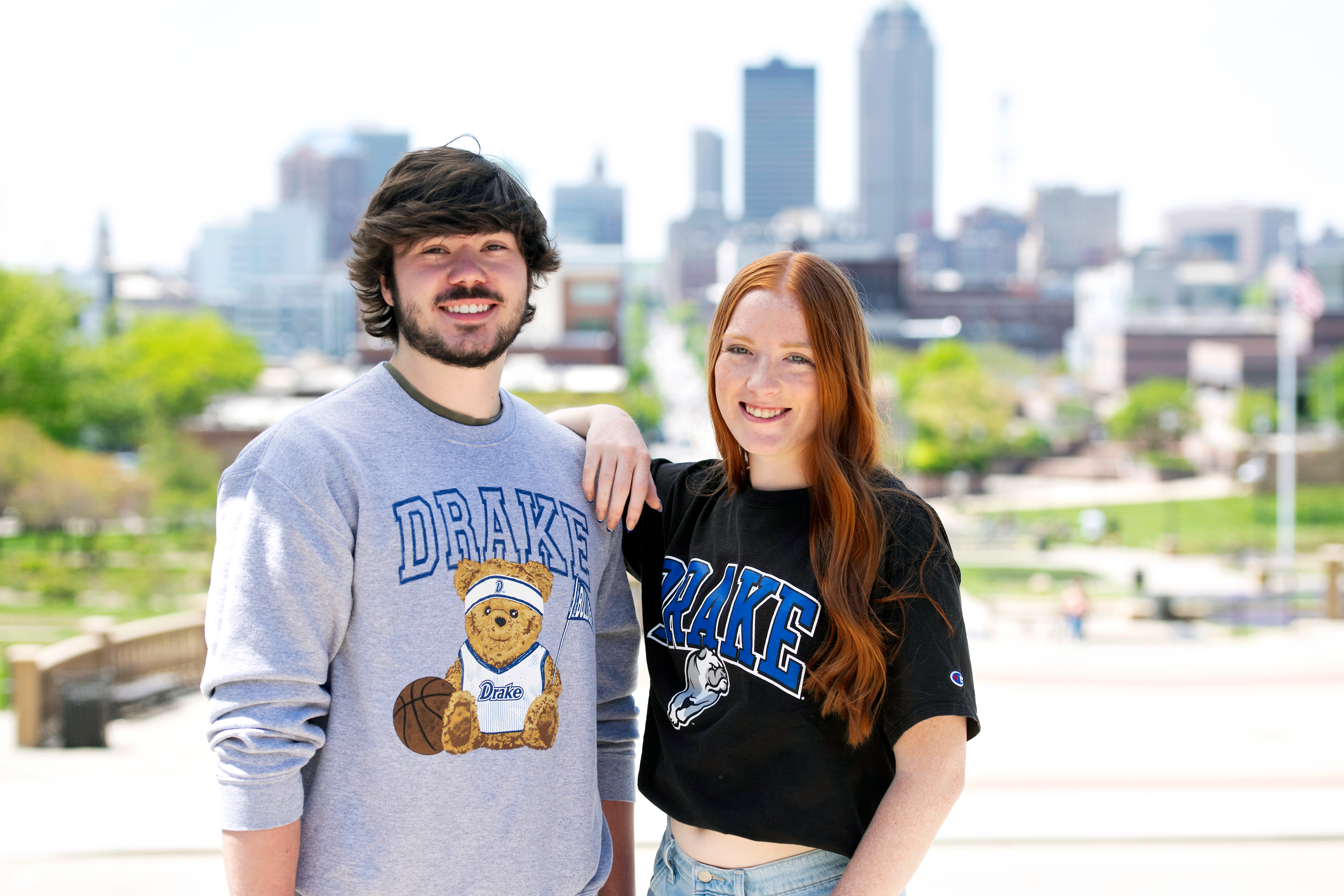 Two Drake students in school shirts pose in front of the Des Moines skyline