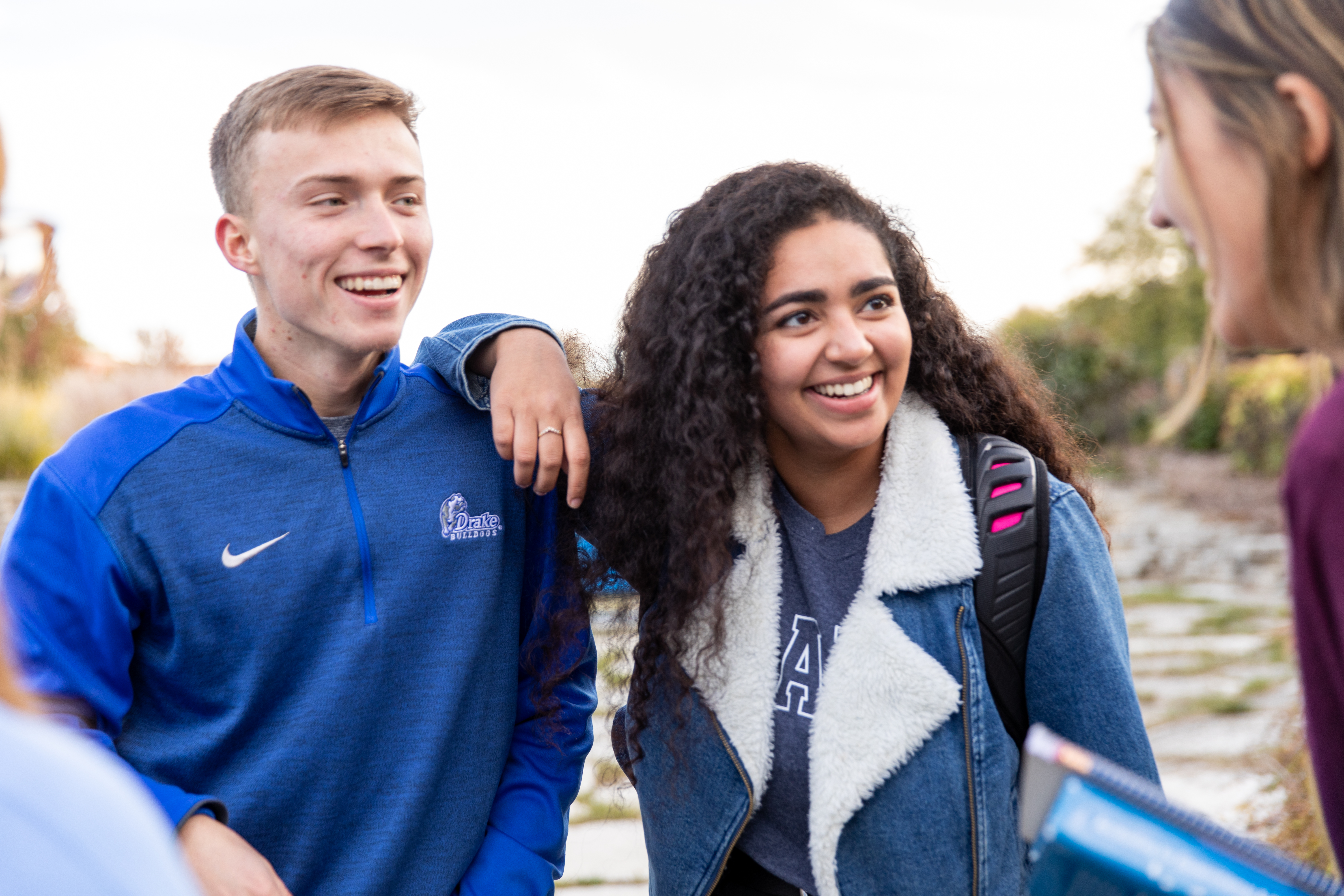 Two Drake students, arm in arm, intently listen to a speaker during a fall campus tour