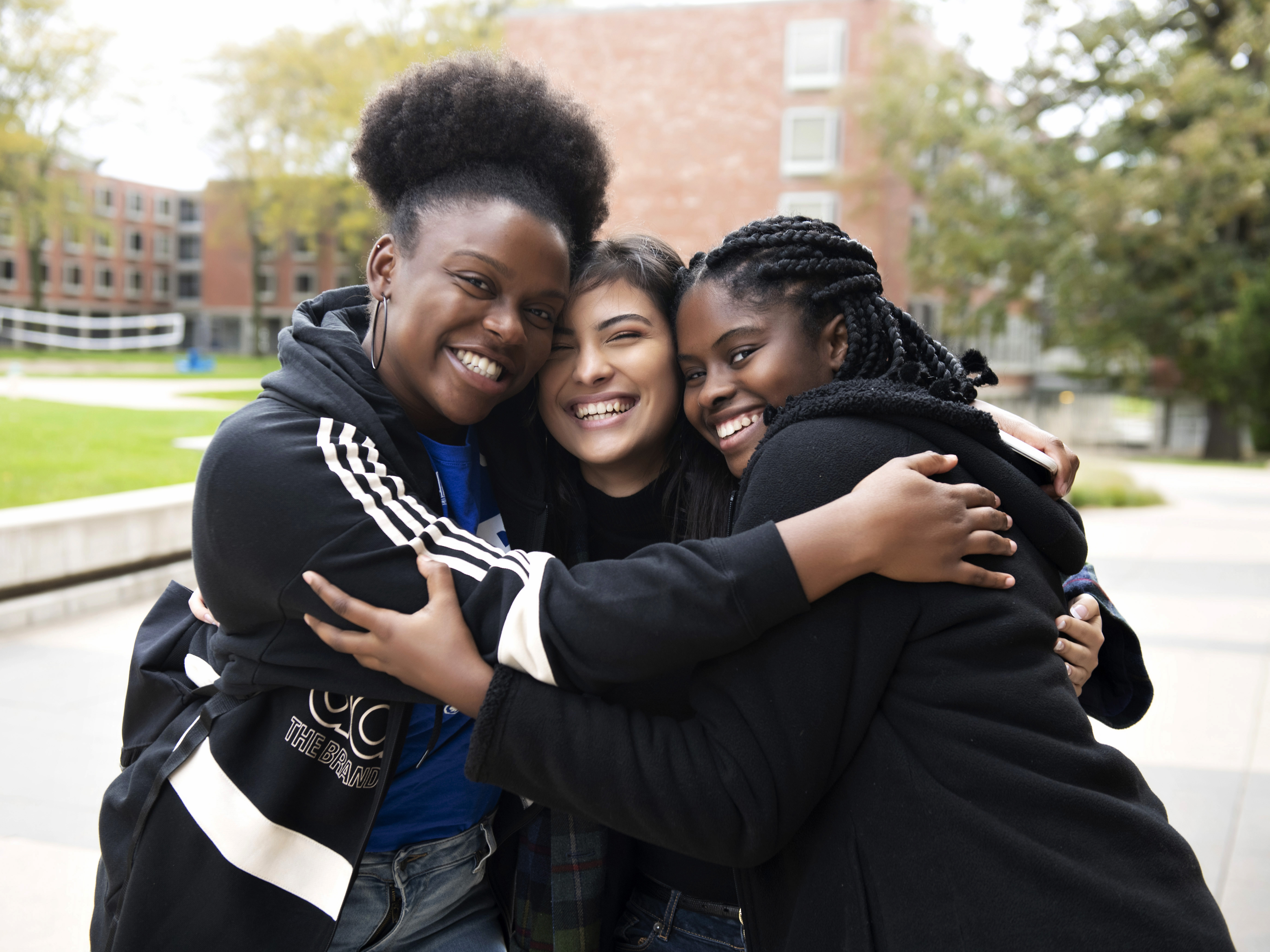 Three Drake students engage in a close hug on a pathway near student housing