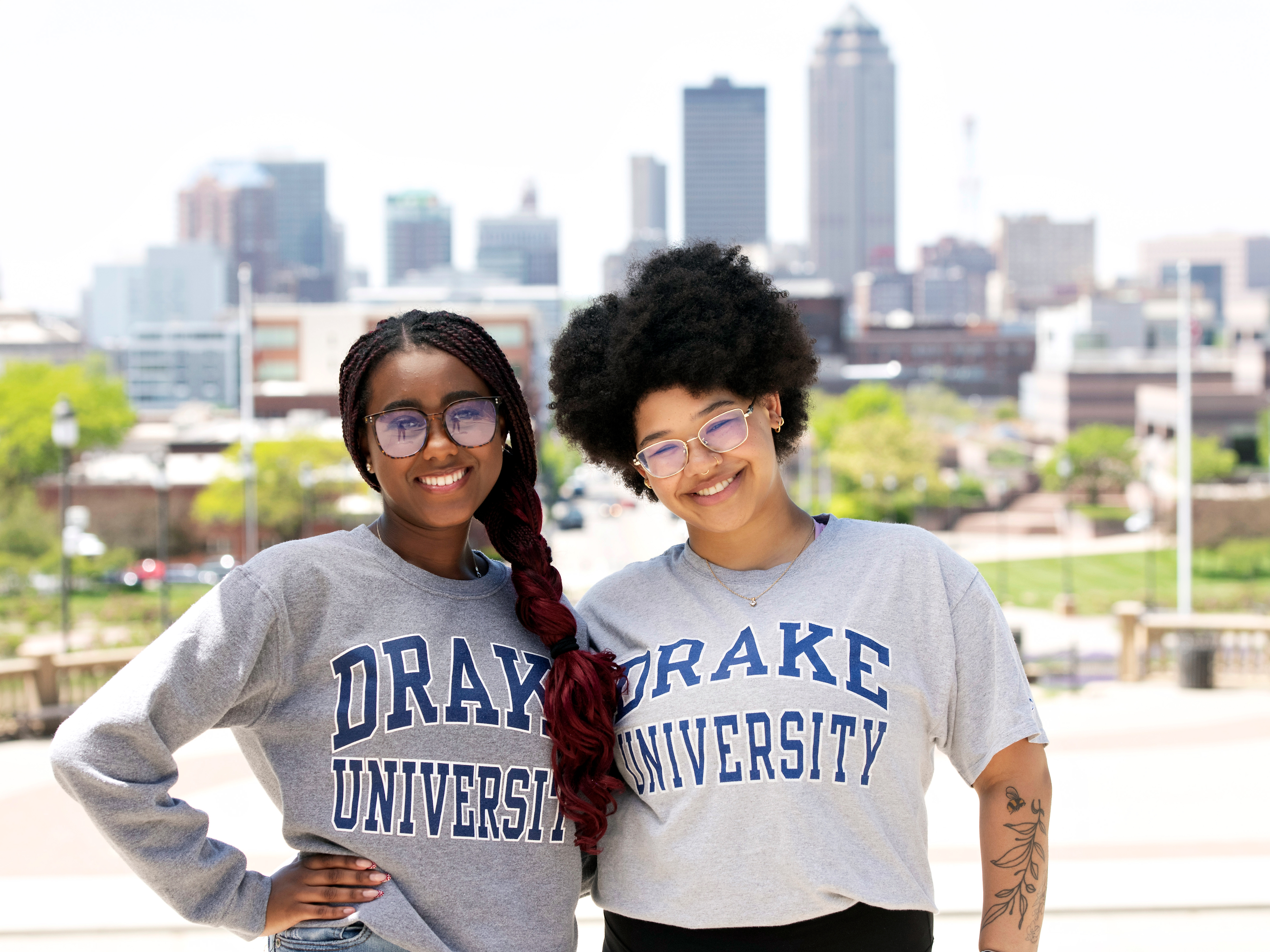 Two students in Drake gear stand together with the Des Moines skyline in the background