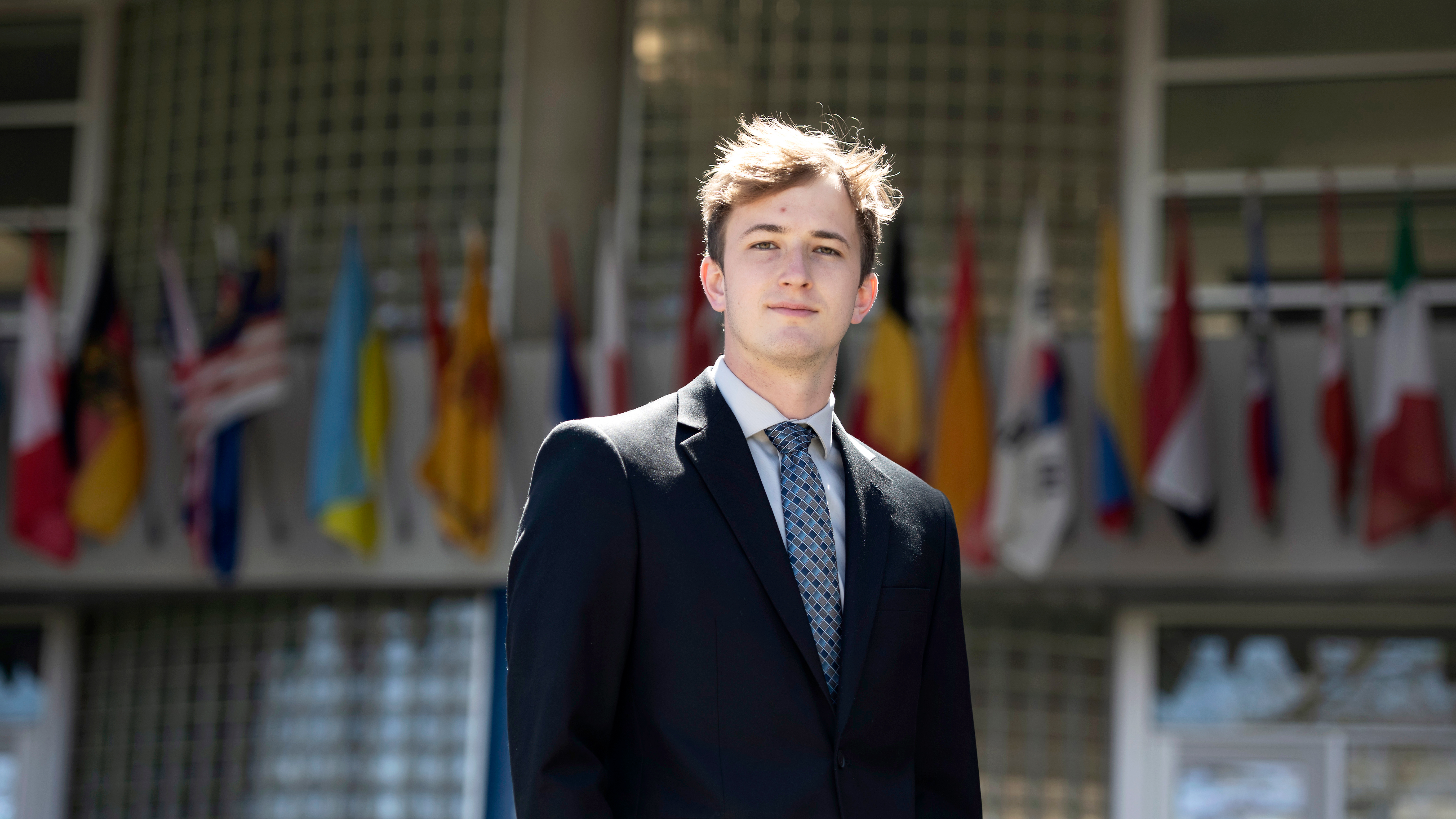 A Drake student wearing a suit stands in front of a building with international flags on the outside