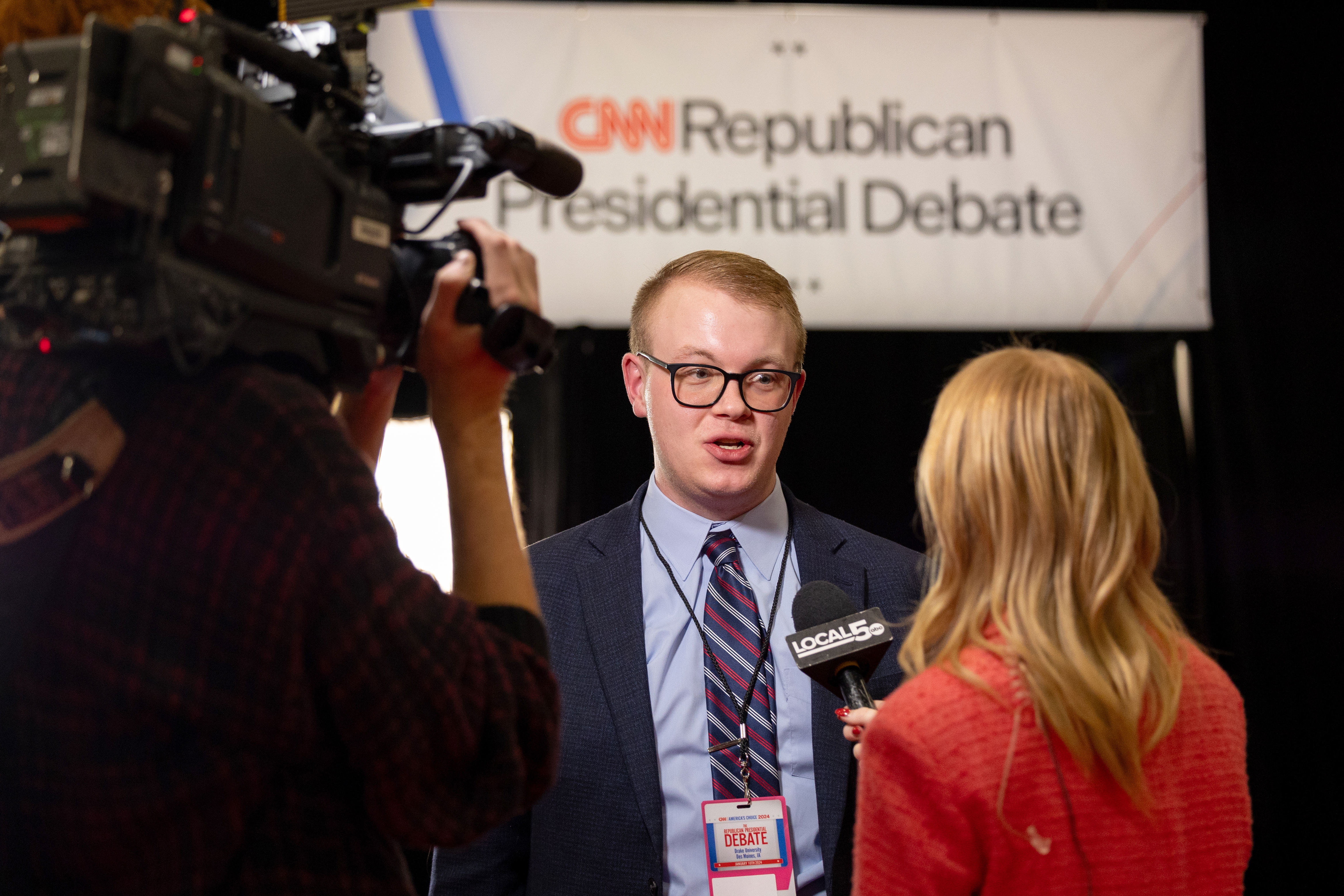 A Drake student in a suit and press pass speaks with a local news station during the Republican presidential debate