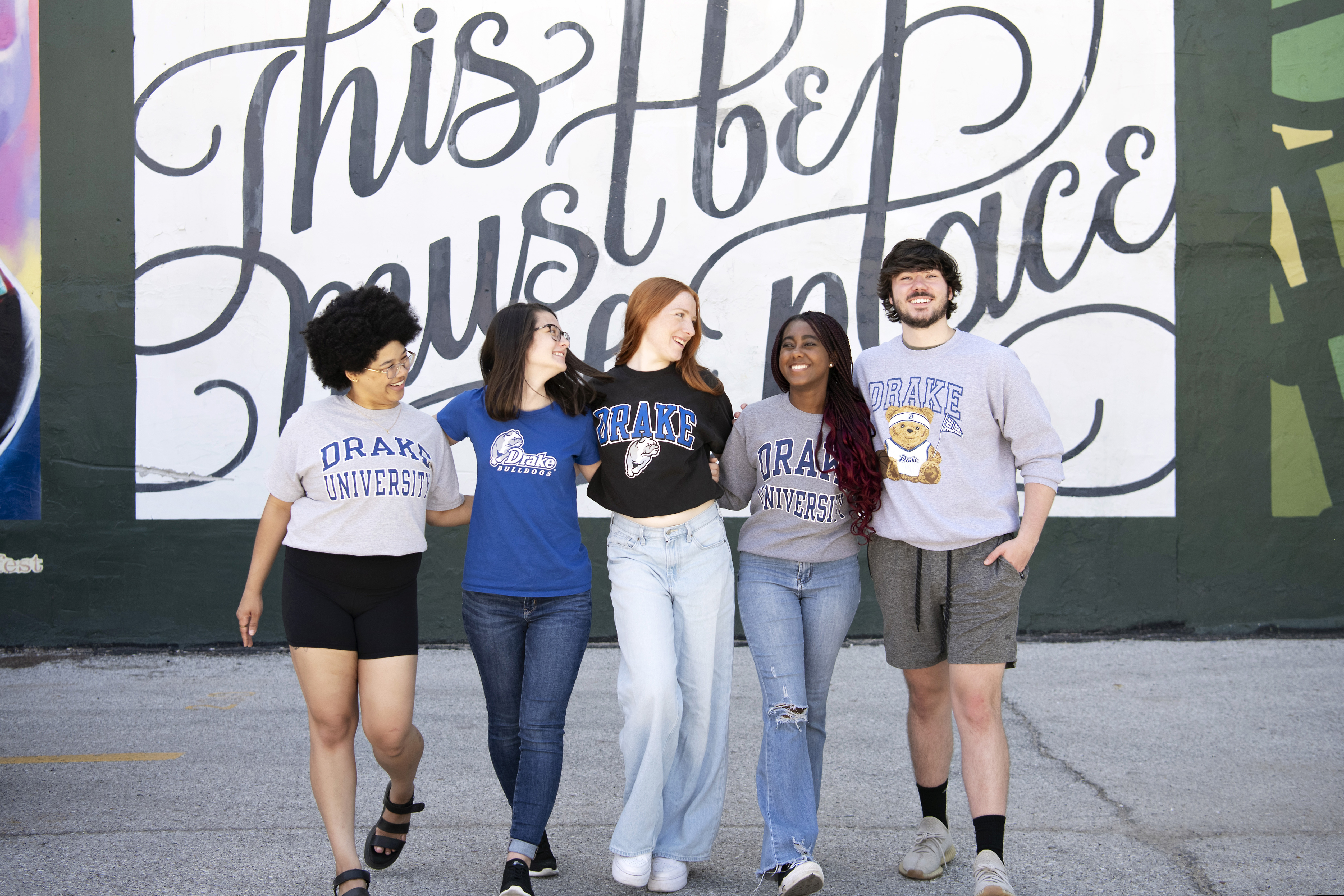 Five Drake students in school shirts stand in front of a mural that reads "This must be the place" in cursive