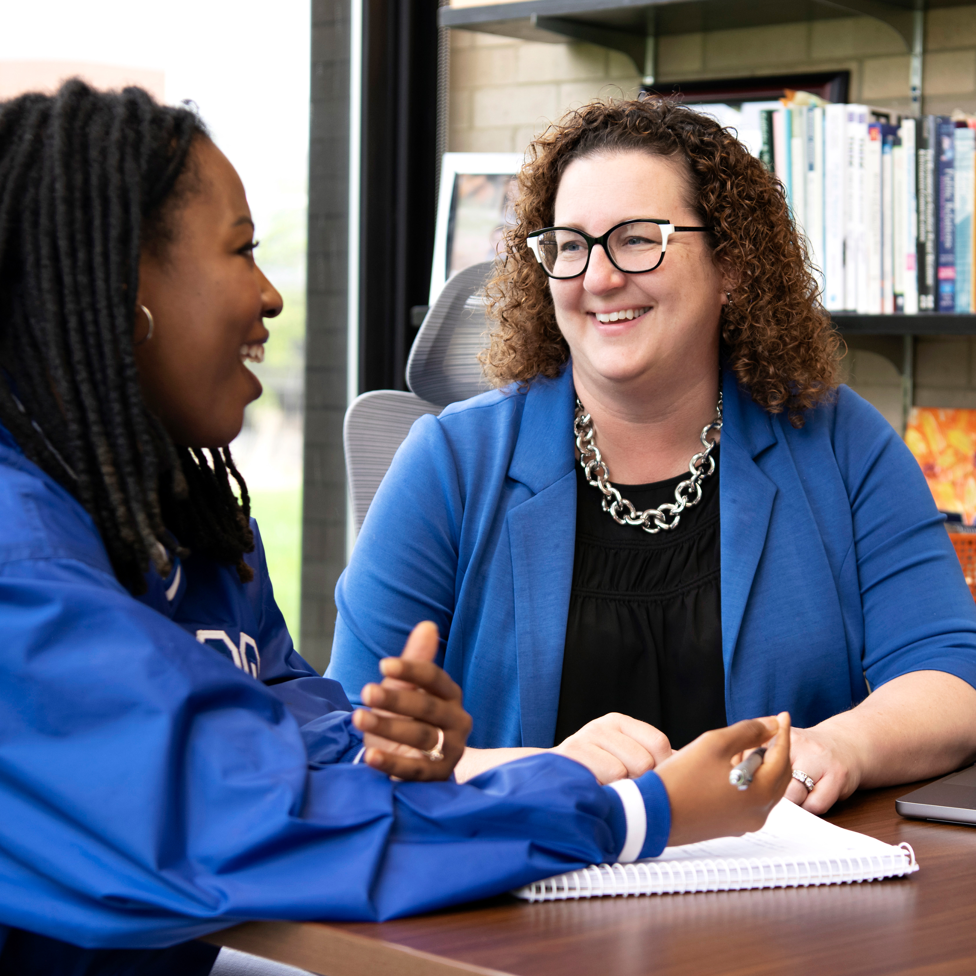 Around a desk, a teacher has an animated discussion with a student, who's 