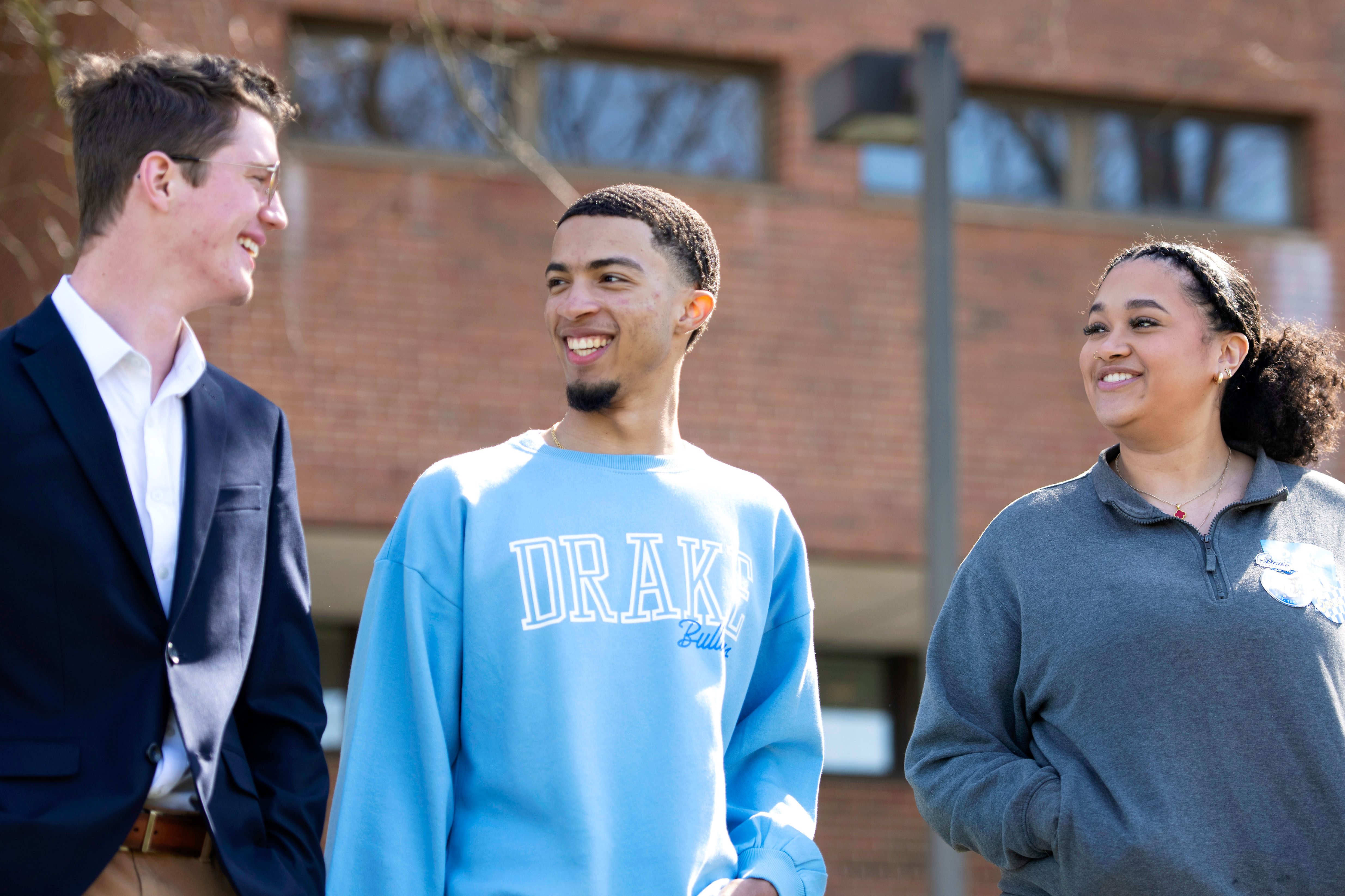 A Drake Personal Mentorship Peer Mentor has a discussion with two students outdoors in front of a brick building