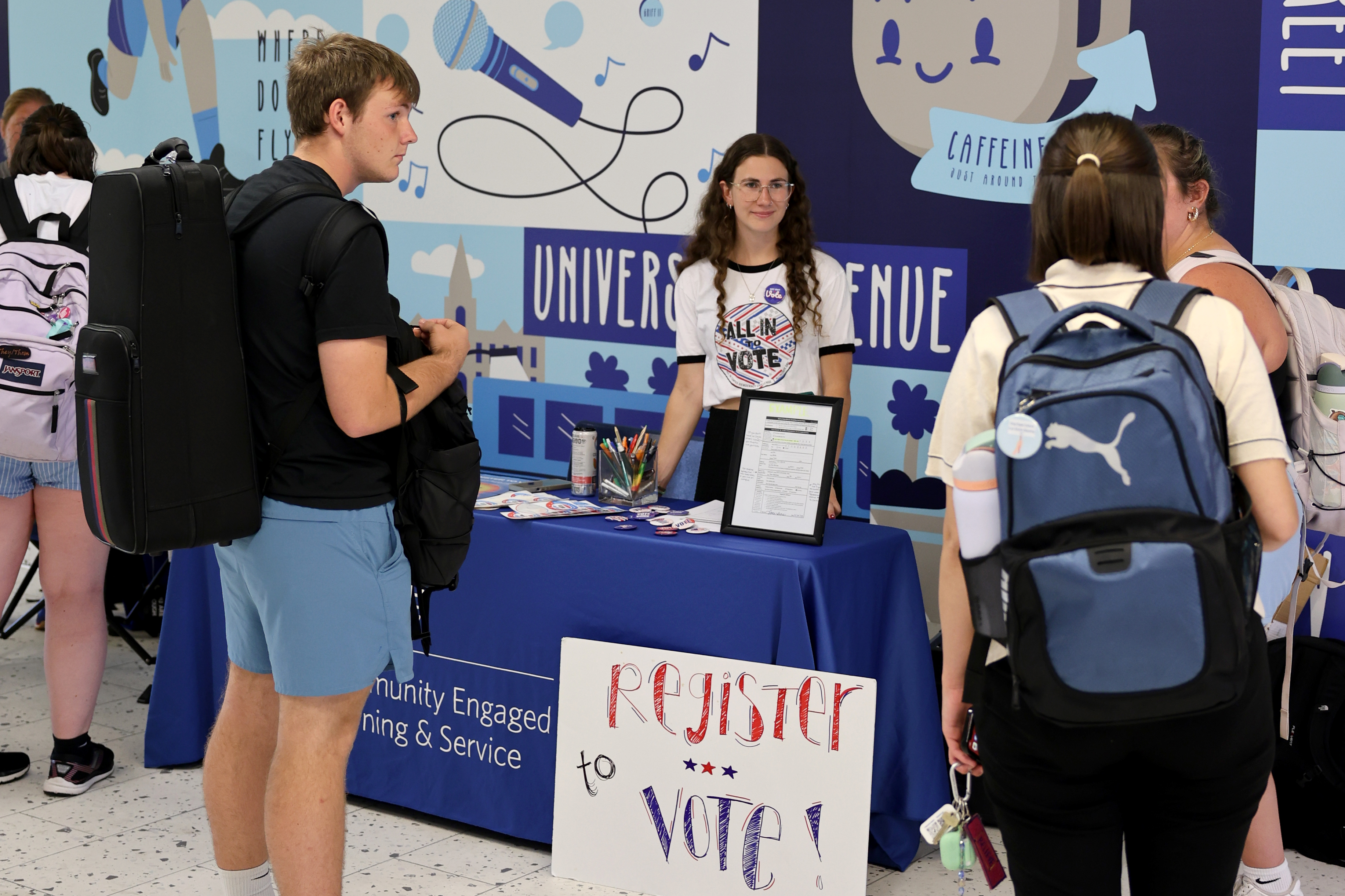 Standing in front of a patterned blue and gray wall, Drake students set up a table to register fellow students to vote