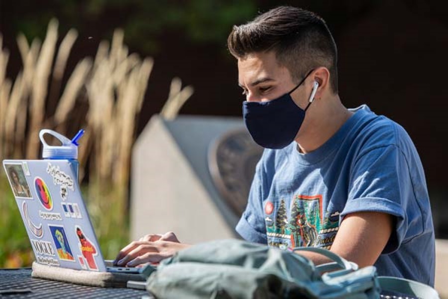 Student typing on laptop at an outdoor table on campus