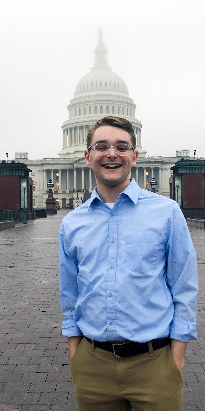 A student in business attire stands in front of the U.S. Capitol building