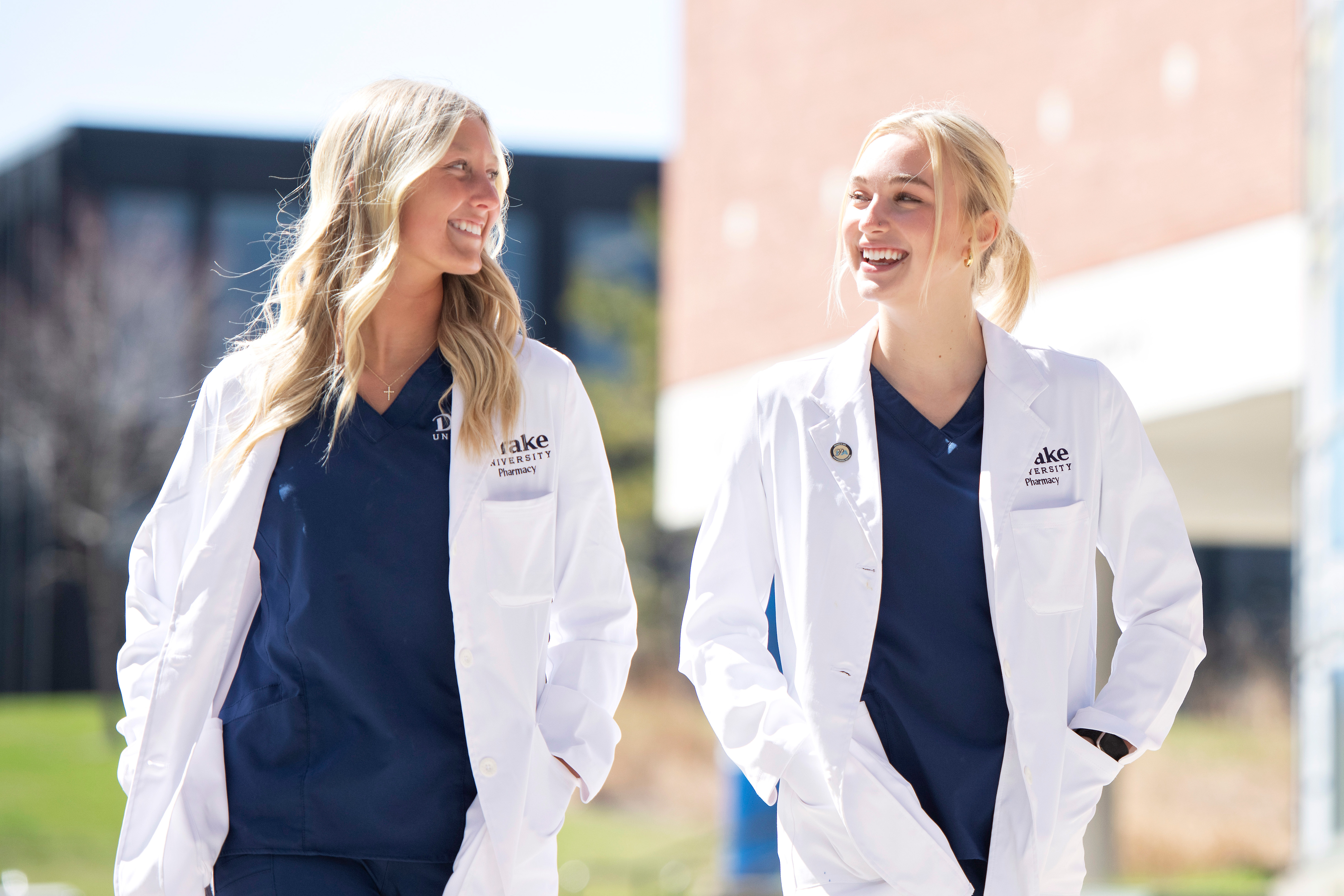 Drake College of Pharmacy and Health Sciences students in school-branded lab coats and blue scrubs go for a walk through campus