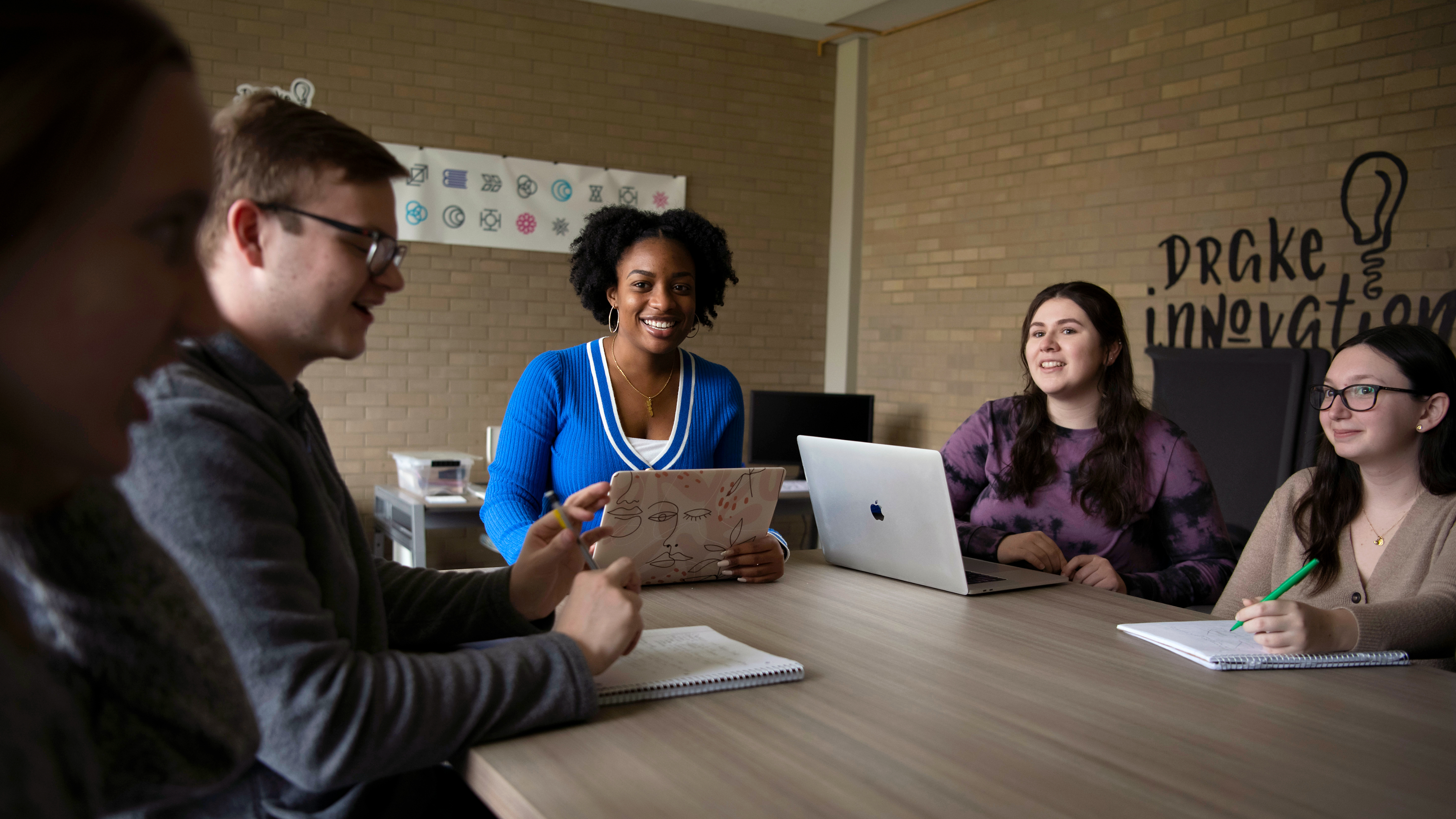 Around a table with laptops, a group of Drake students meet to discuss a project in the campus innovation space