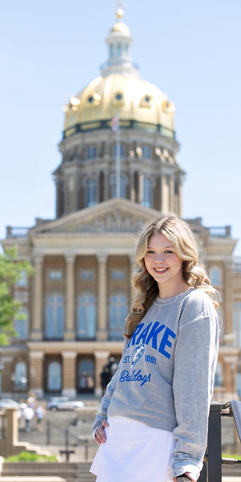 A student in a Drake sweatshirt stands in front of a government building on a sunny day