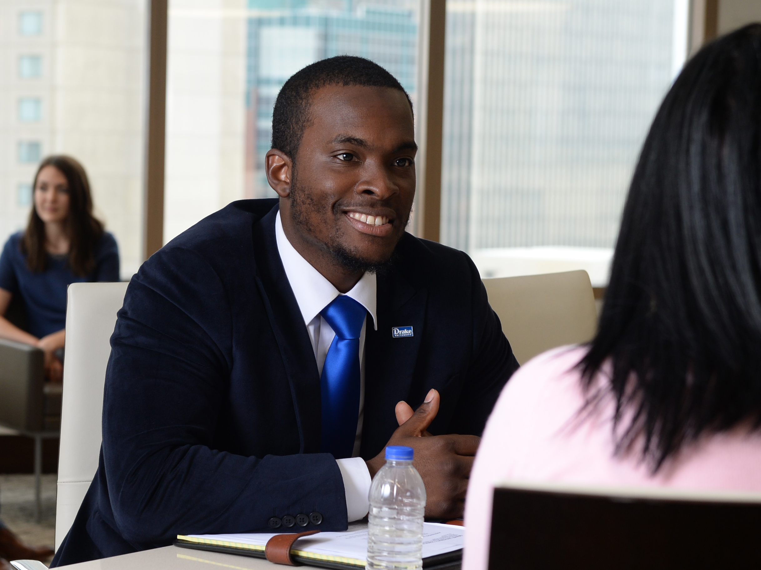 A student in business attire smiles at someone across a table