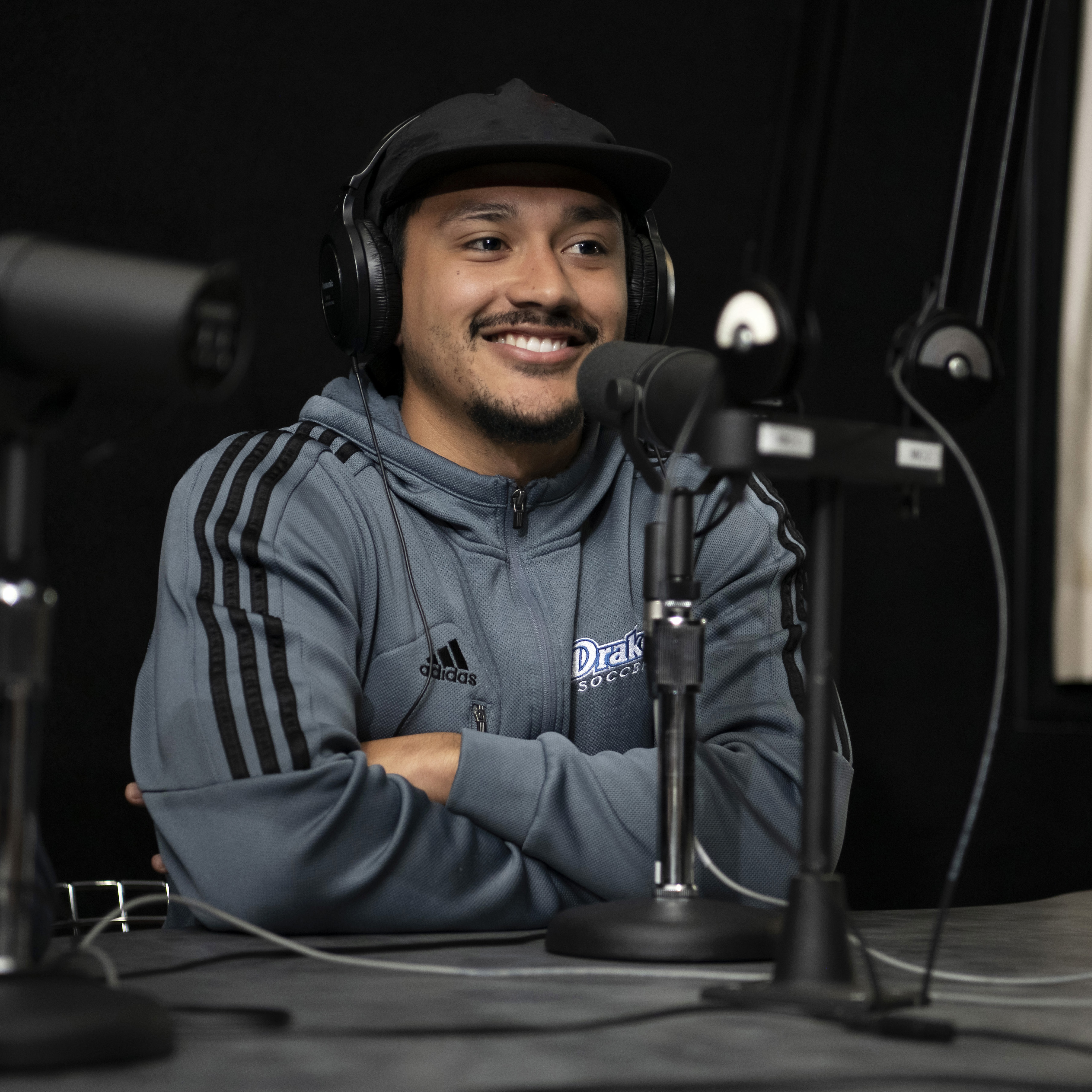 A student wearing headphones smiles while sitting in front of a microphone