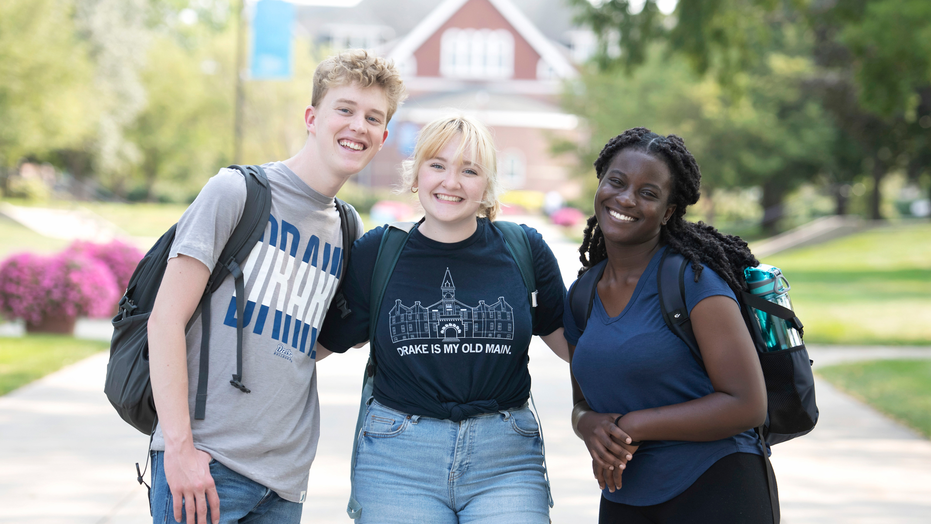 Three students wearing backpacks pose with arms around each other and smile at the camera