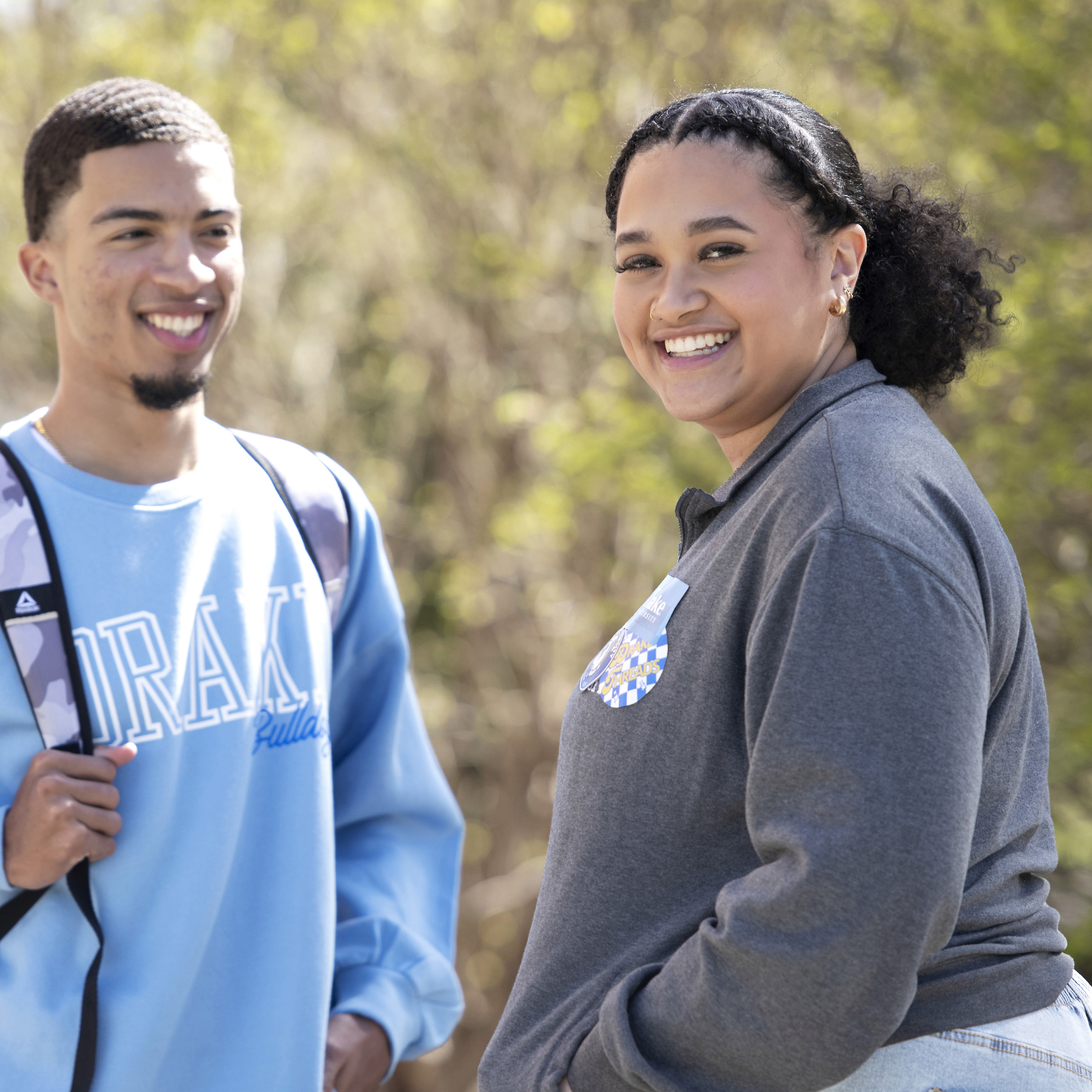 Two students stand, speaking and smiling outside on campus