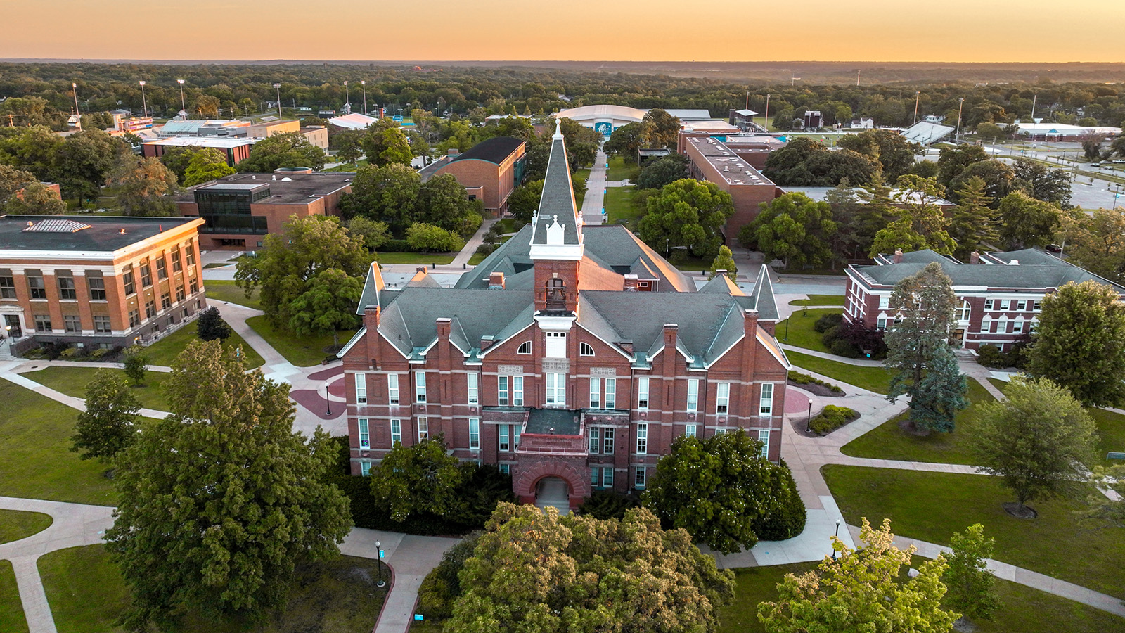 Aerial view of Drake University's campus hovering over Old Main, with an orange sunset in the background.