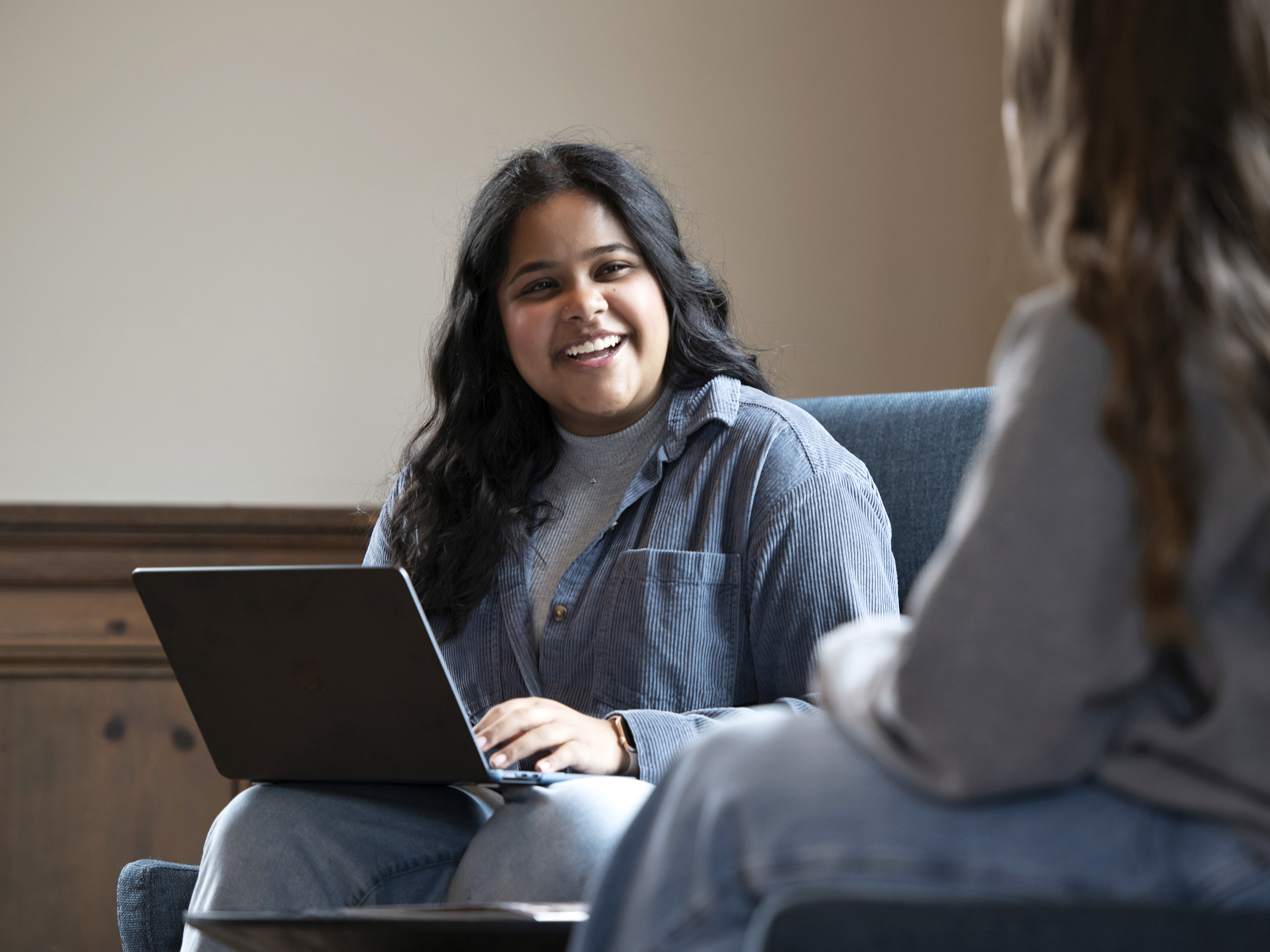 Two Drake students meet in a common area, one supporting a laptop