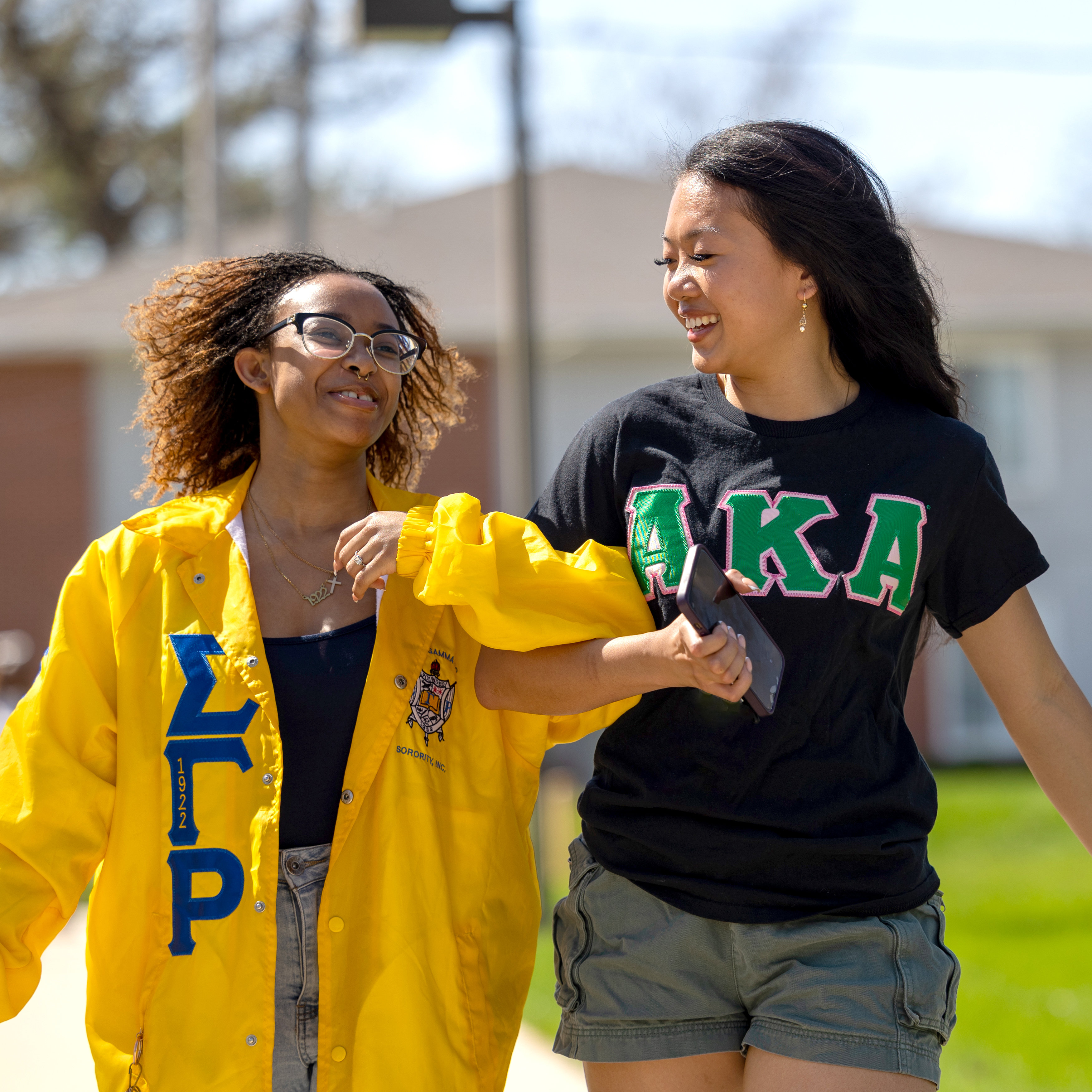Two Drake student wearing clothing with Greek letters lock arms as they walk through campus