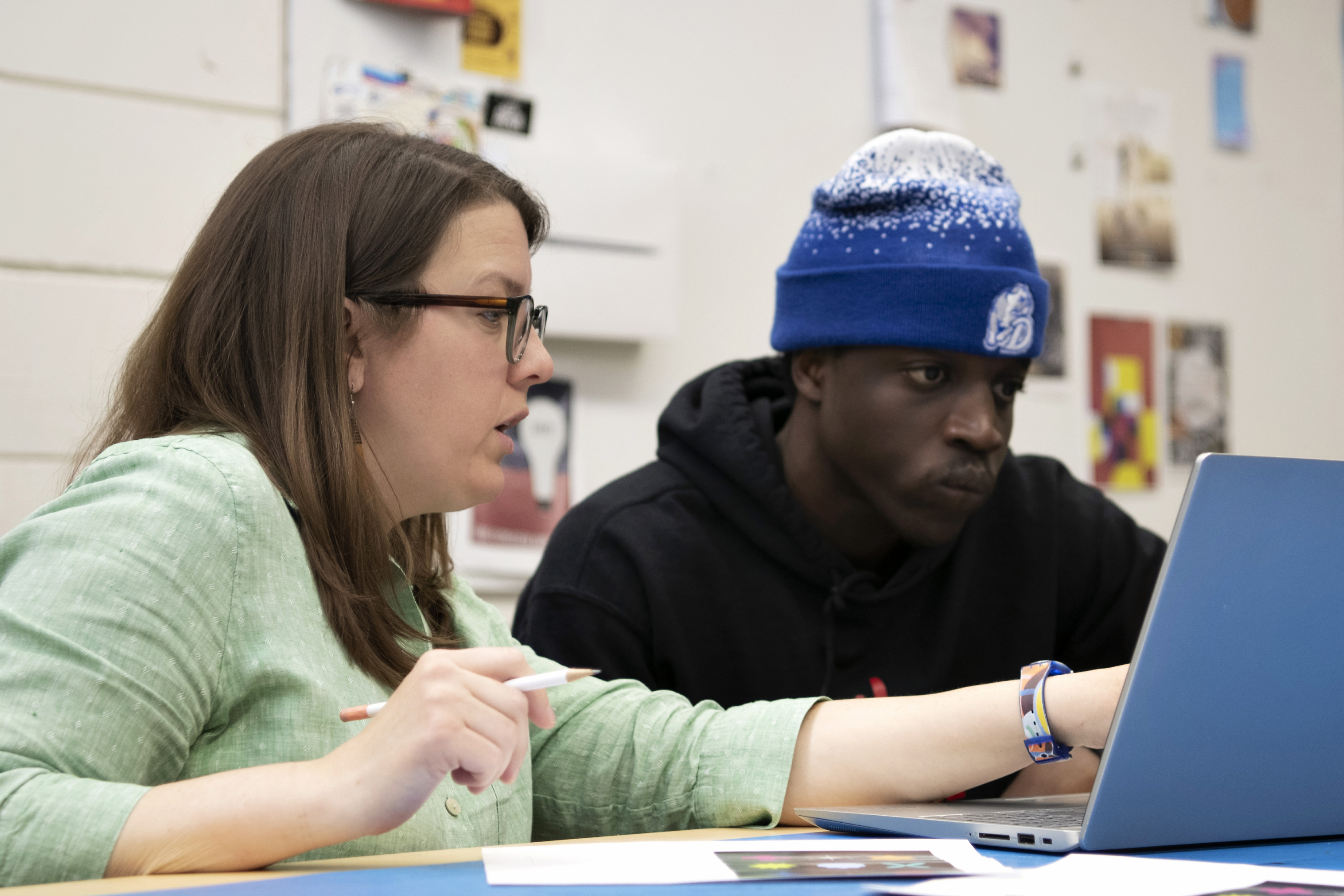 In a campus art studio, a faculty member critiques a student's assignment displayed on a laptop screen