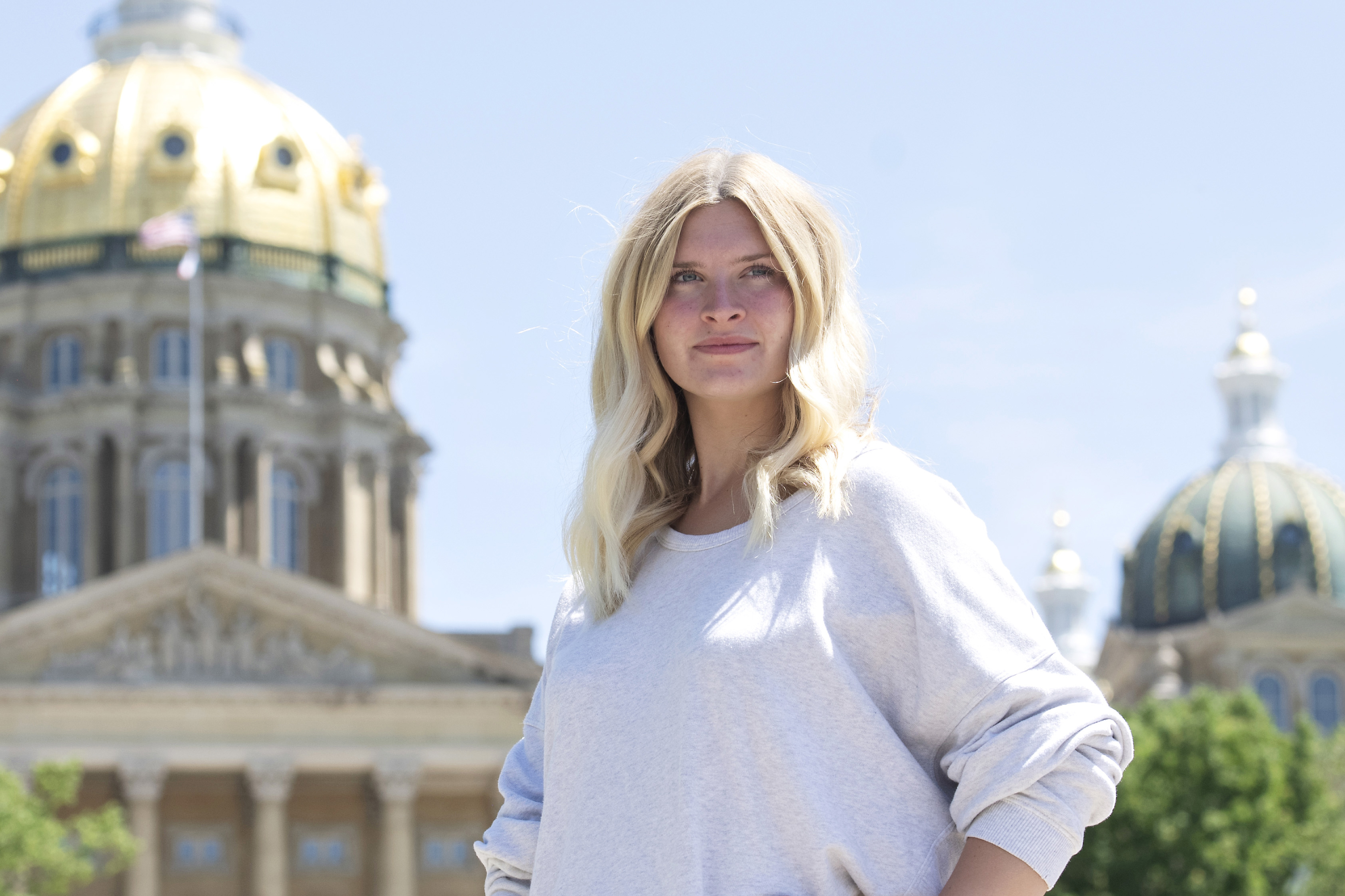 A Drake graduate student stands, hands on their hips, near the Capitol building in Des Moines