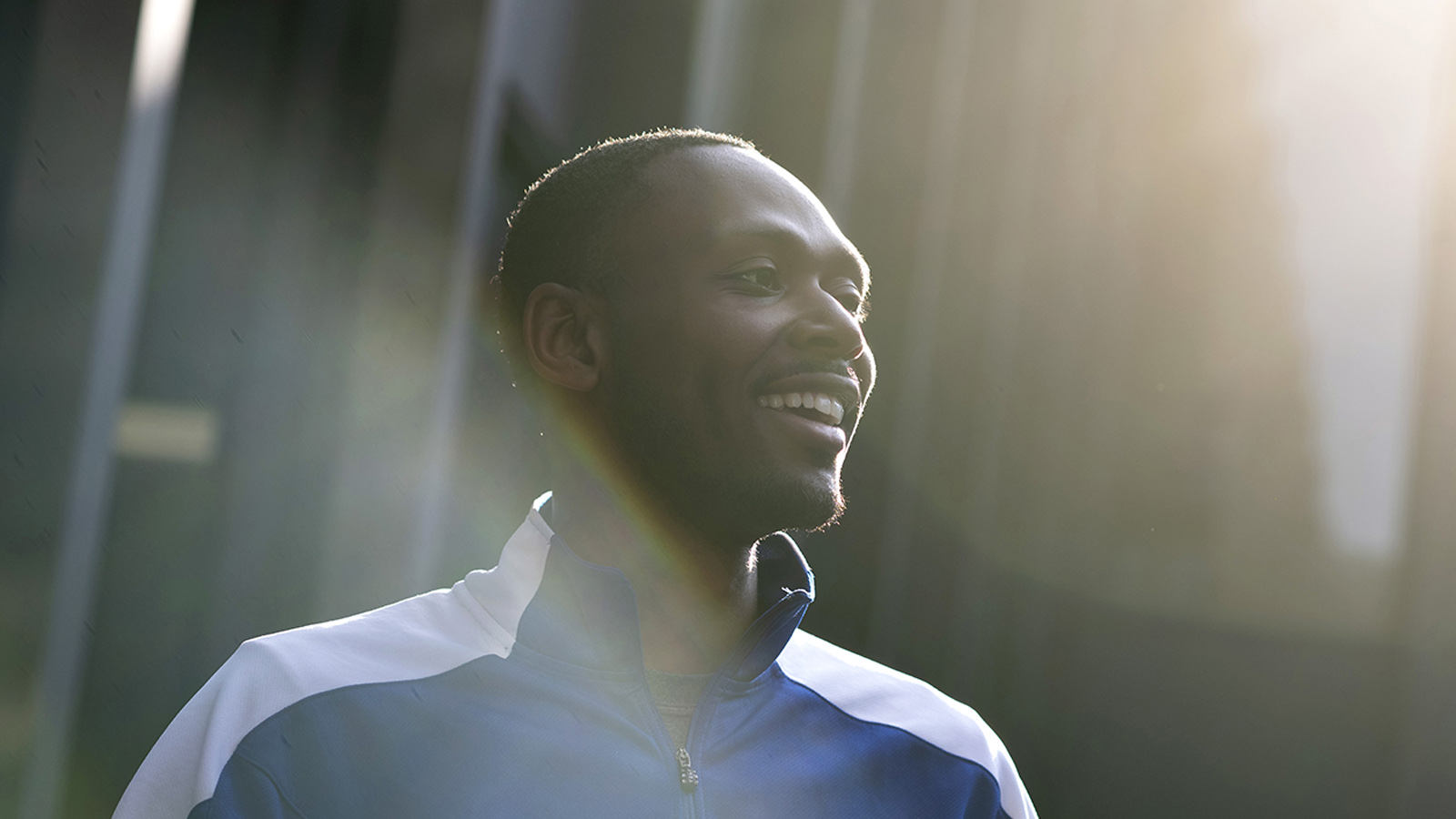 A Drake student smiles in the sunlight outdoors while wearing a Bulldogs track jacket