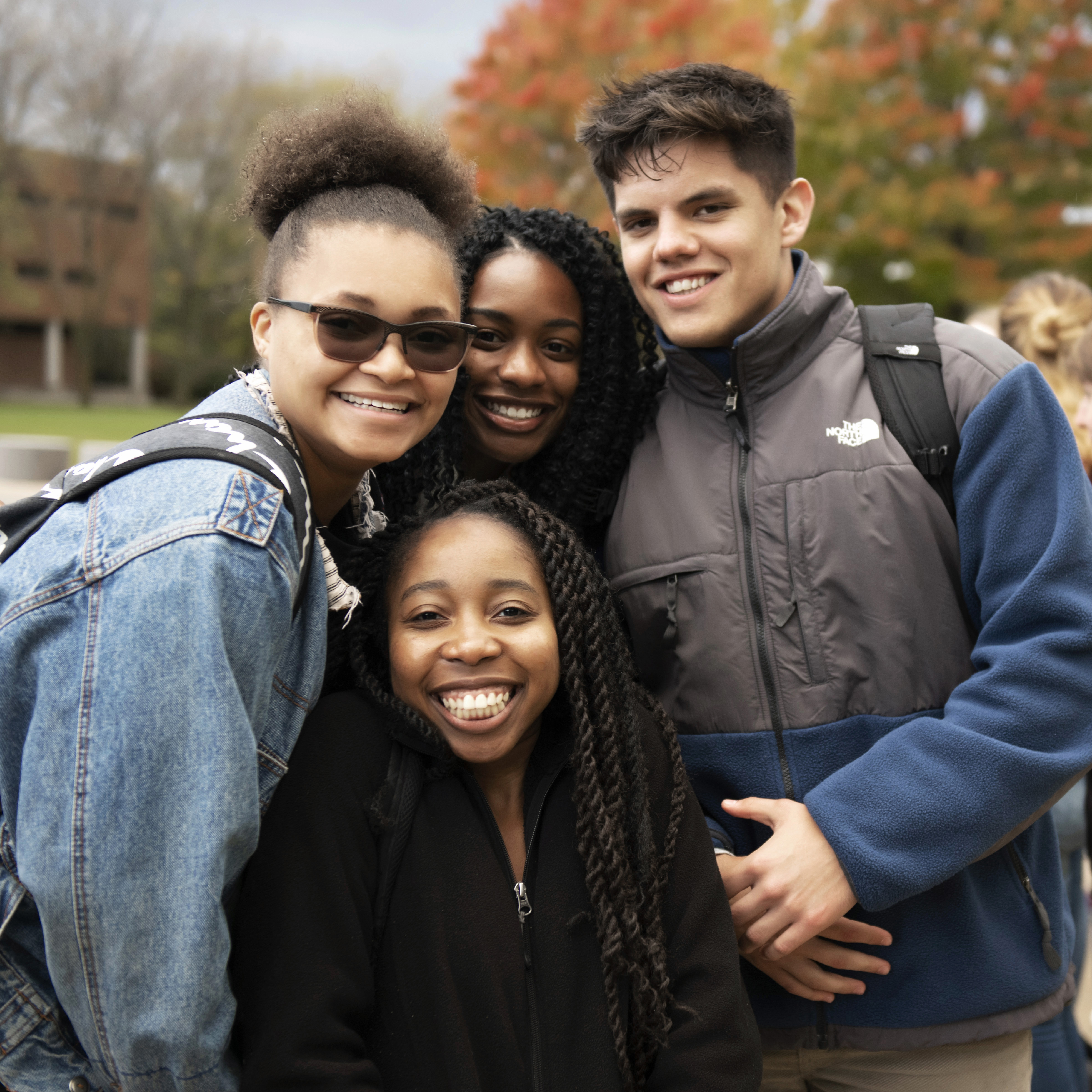 A group of Drake international students in light jackets and pullovers huddle close on a fall afternoon