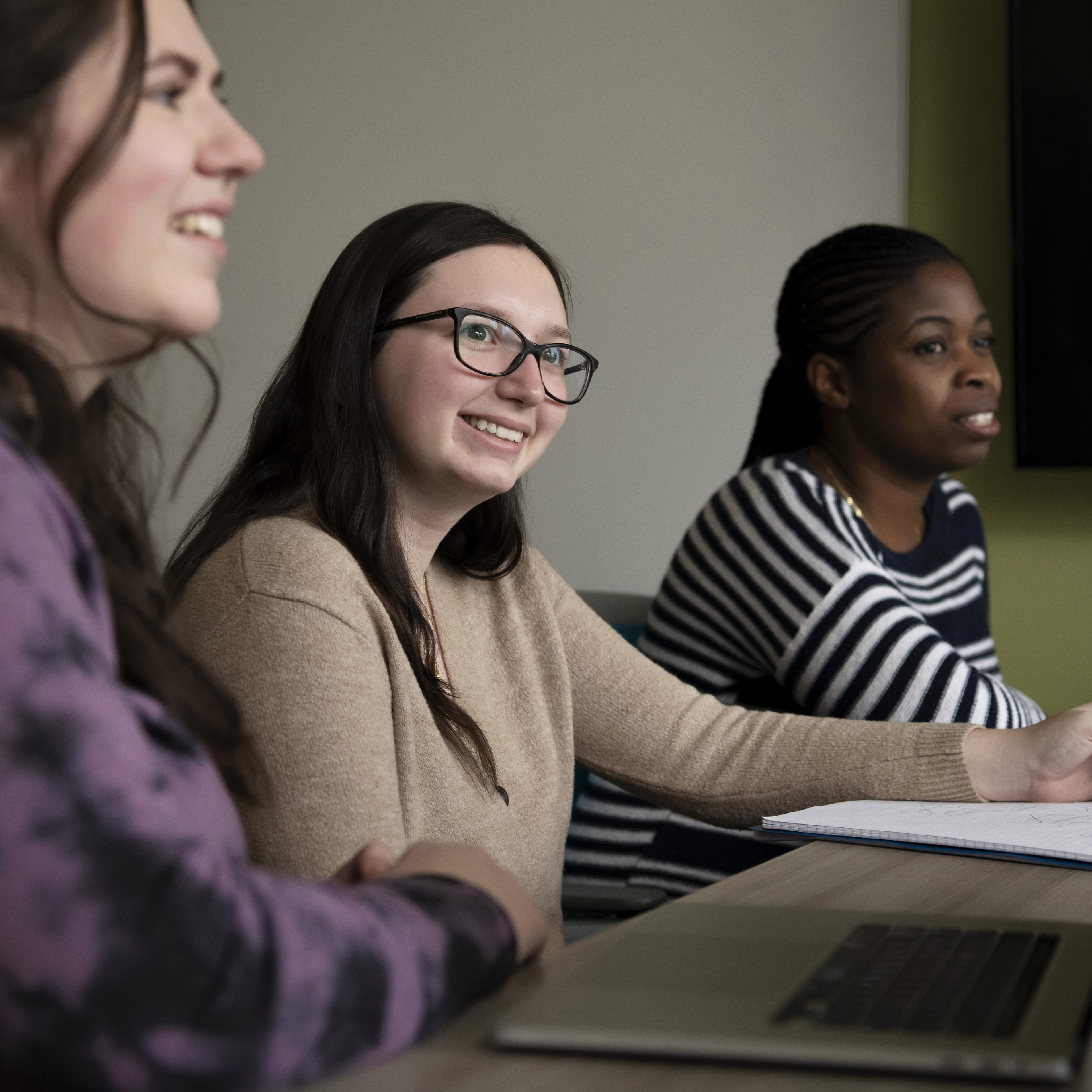 Students behind a desk listen and smile during a class at Drake