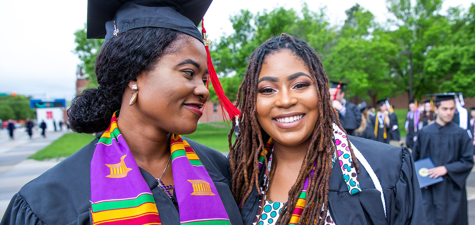 Two Black students in caps and gowns at a graduation ceremony