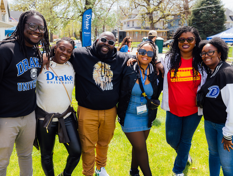A group of Drake alumni link arms and smile outdoors during a scheduled alumni event.