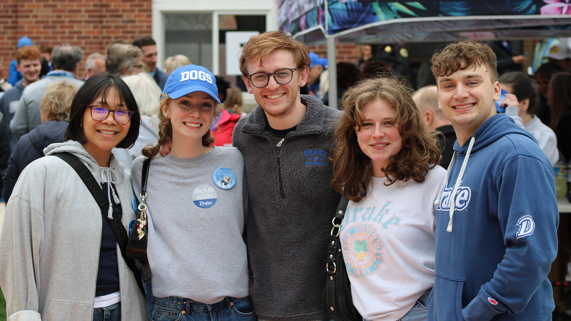 Drake alumni in school gear gather arm in arm during a campus event