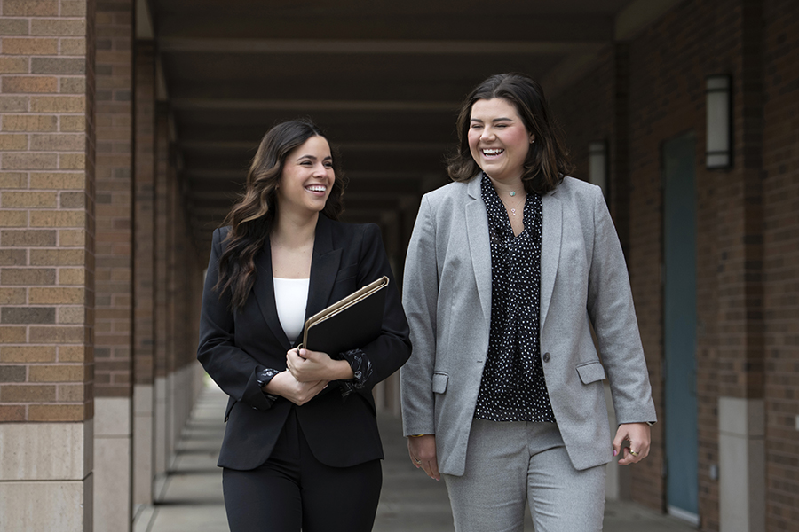 Two Drake alumni in suits converse as they walk through a covered walkway on campus