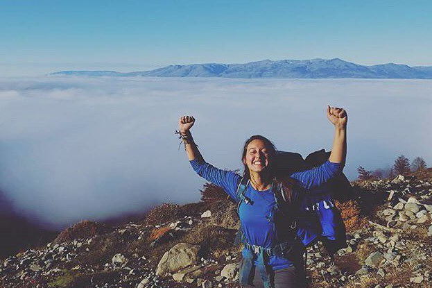 A student with fists raised in triumph on a hike with mountains in the background