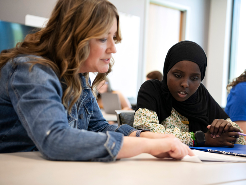 A professor speaks with a student while looking at a paper on a table
