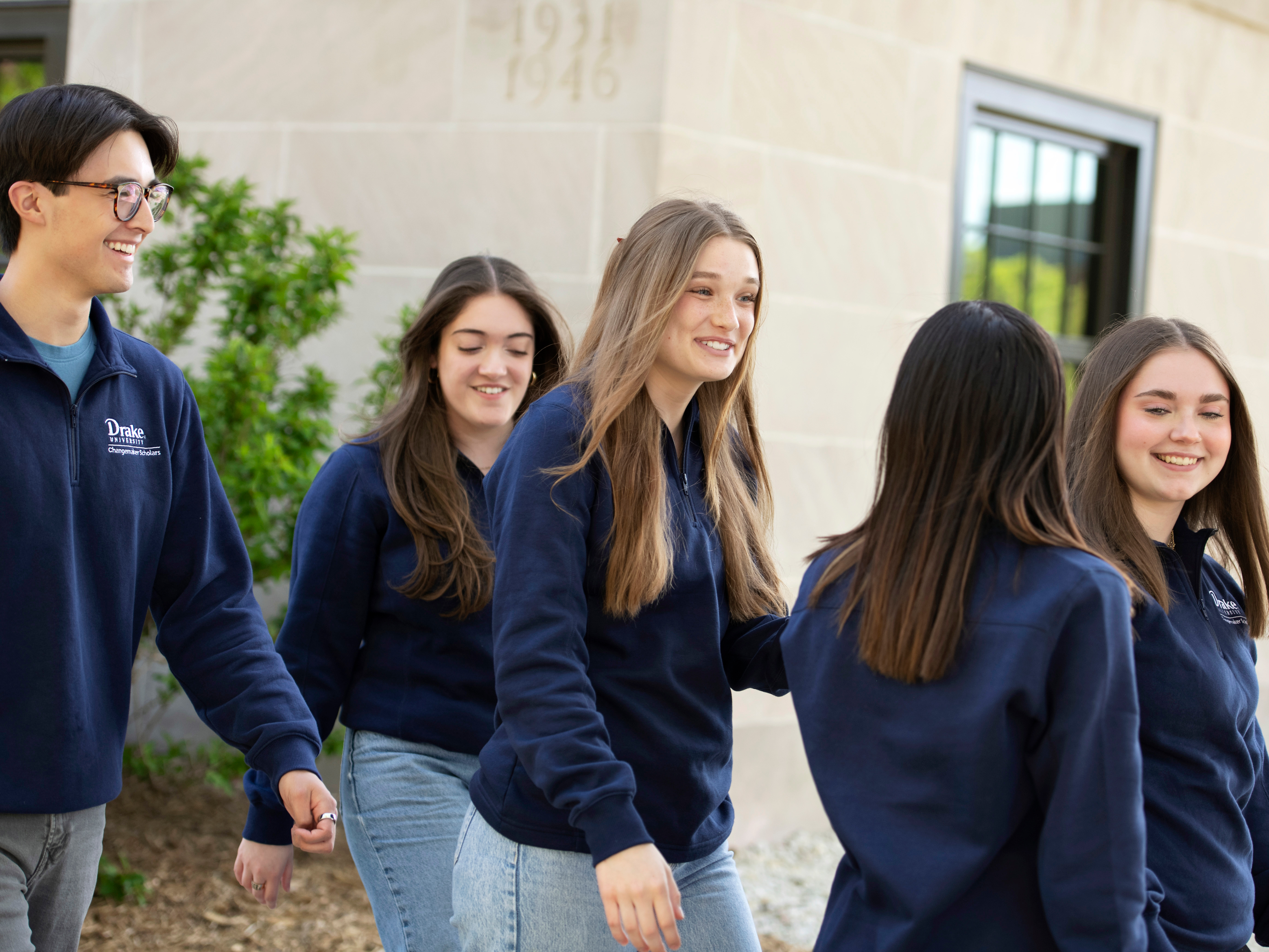 A group of students in navy blue Drake sweaters hold a meeting while walking outdoors