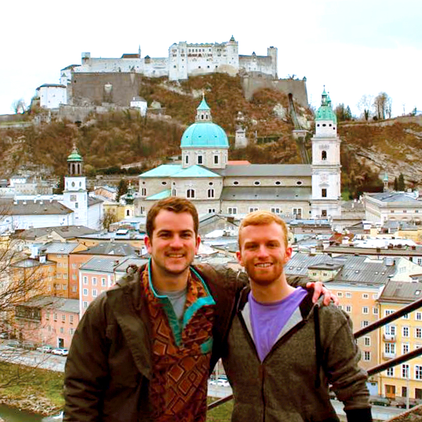During a Drake study abroad trip, two students stand arm in arm in front of mixed buildings constructed in a mountainous area