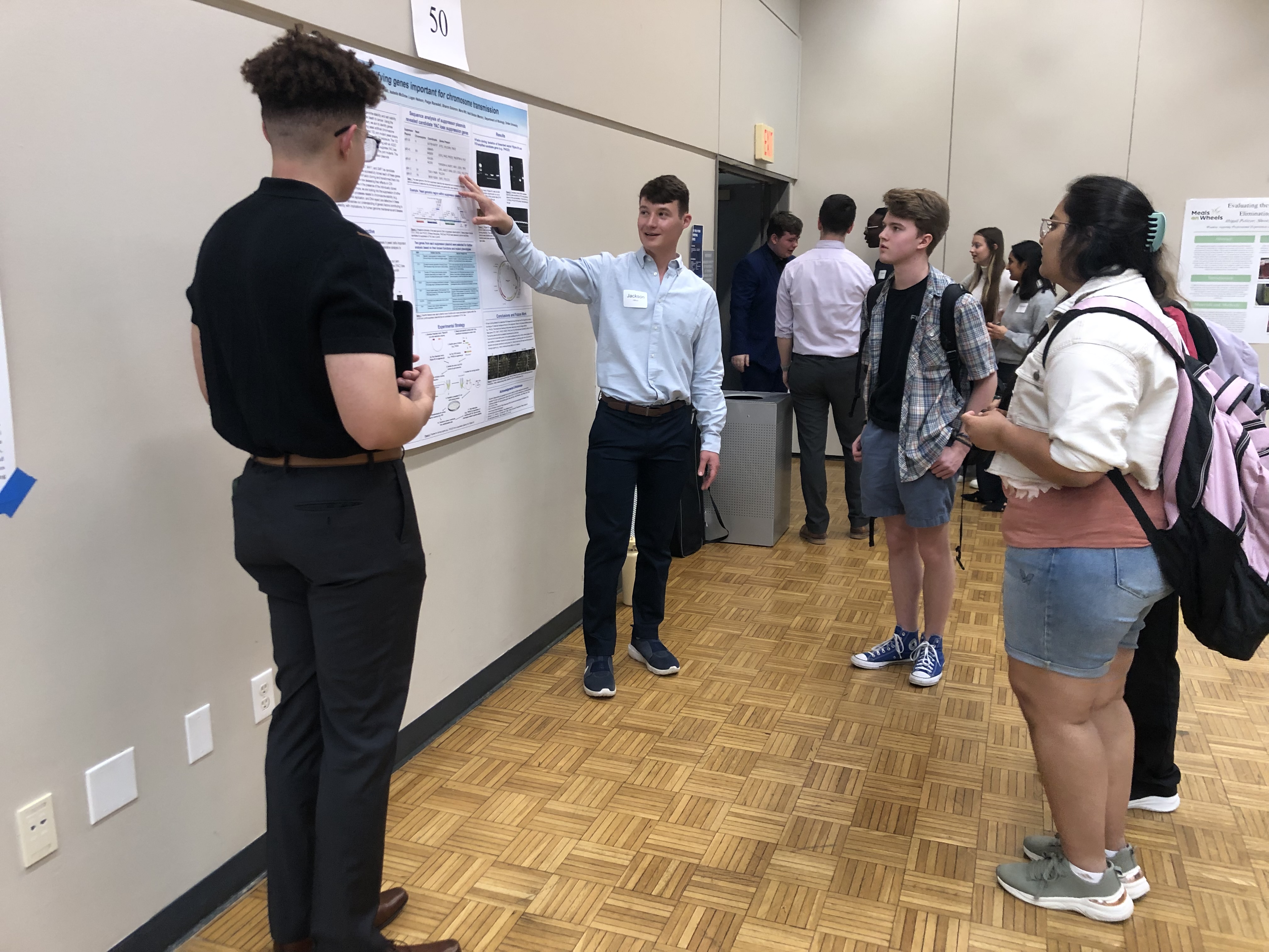 During a presentation to a group of students, a Drake DUSCI undergraduate points to a poster board that highlights their research