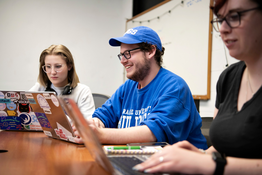 Three students sit at a table smiling with laptops