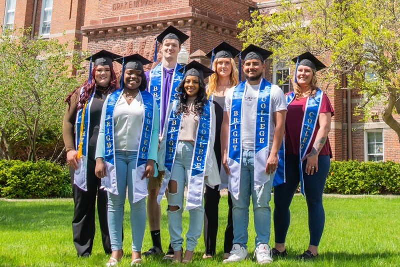 A group of students stand outside on campus in commencement caps and stoles