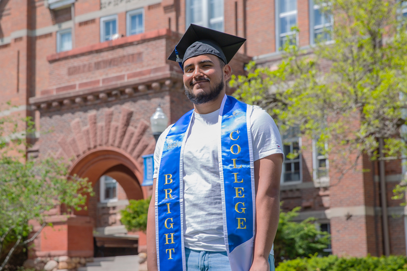 A student stands outside on campus in commencement attire
