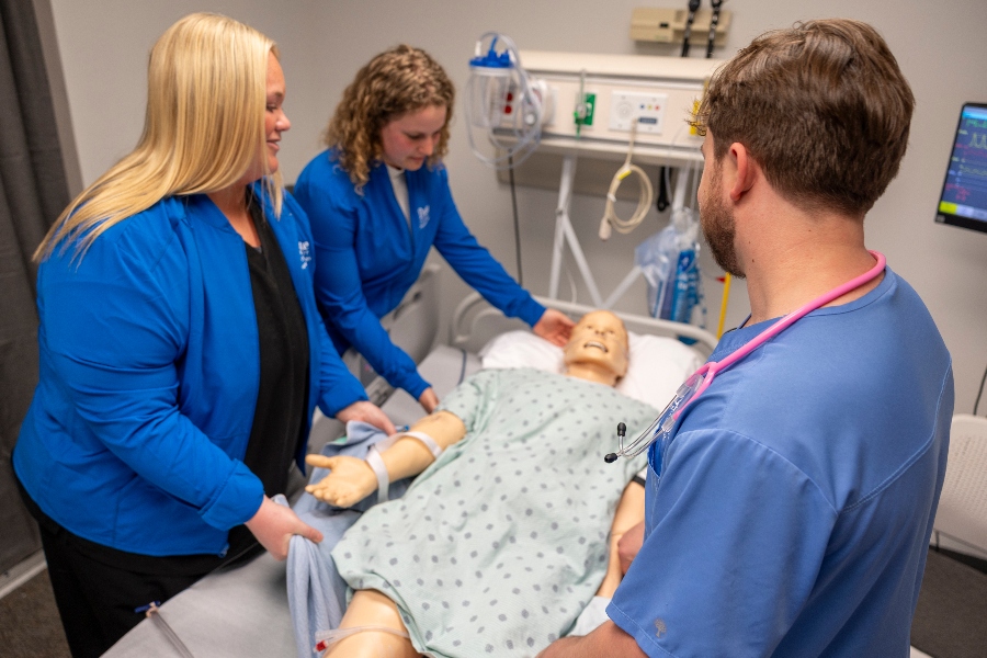 Two Drake OTD students move the limbs of a mannequin in a hospital room