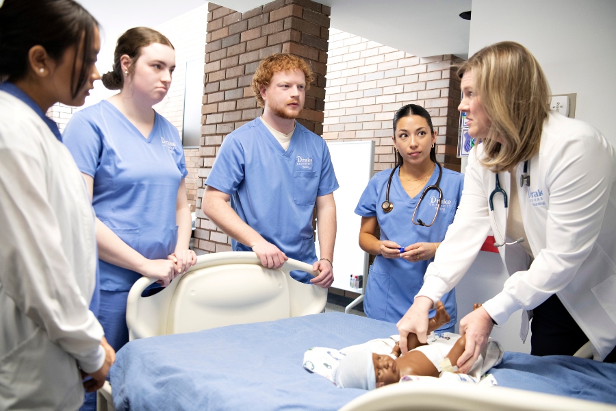 A group of Drake nursing students surround a hospital bed and listen to their instructor