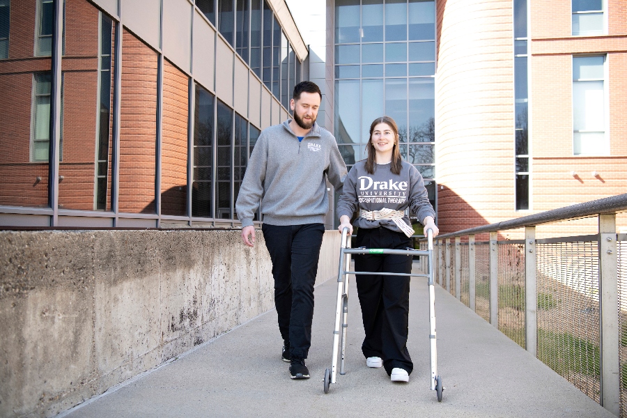 A Drake student helps a classmate walk through campus using a walker and gait belt in a simulation experience