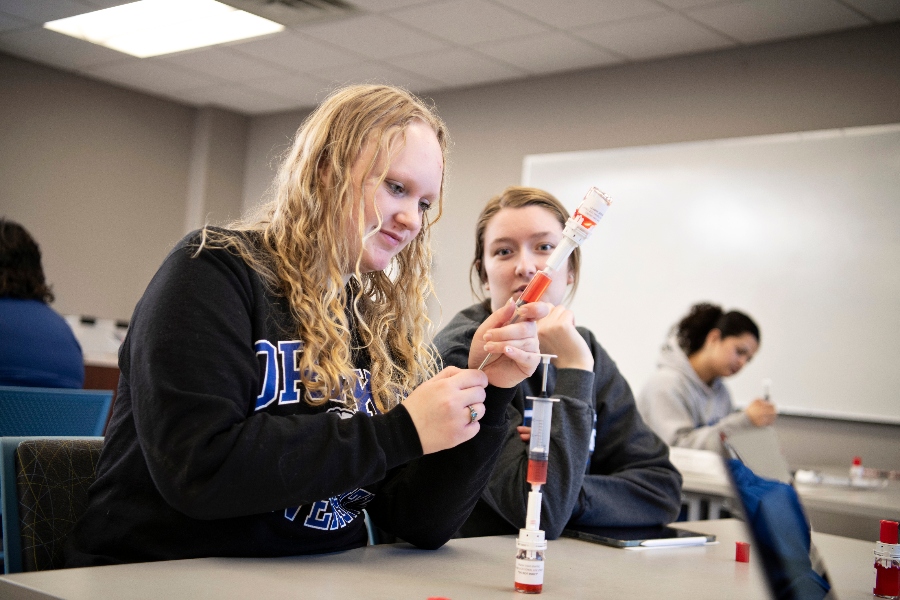 Two Drake students work with a medication and syringe in lab