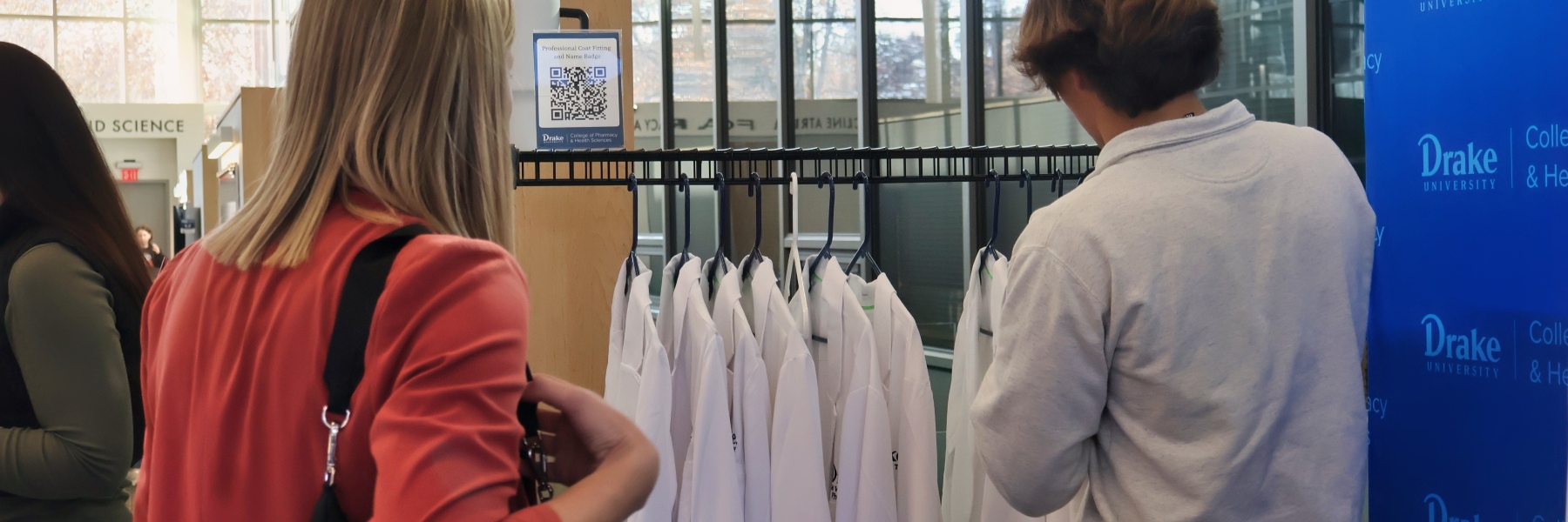 A Drake Pre-Pharmacy student waits to try on a pharmacy white coat from a rack