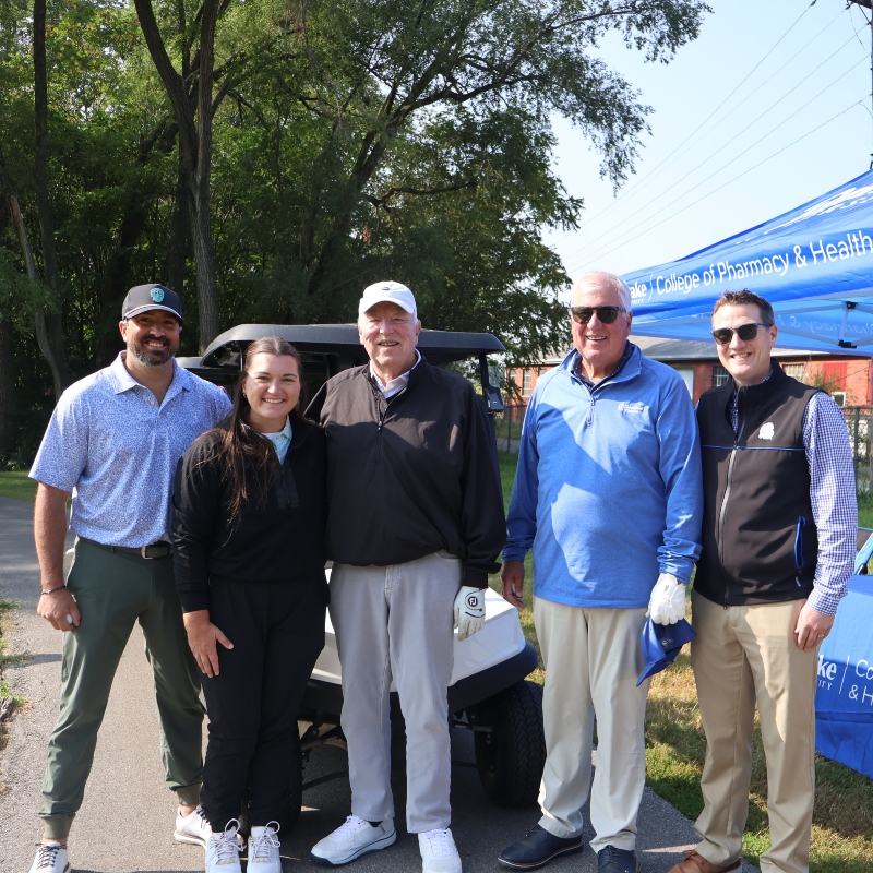 Drake alumni pose with the Dean at the Drake tent at a golf fundraiser